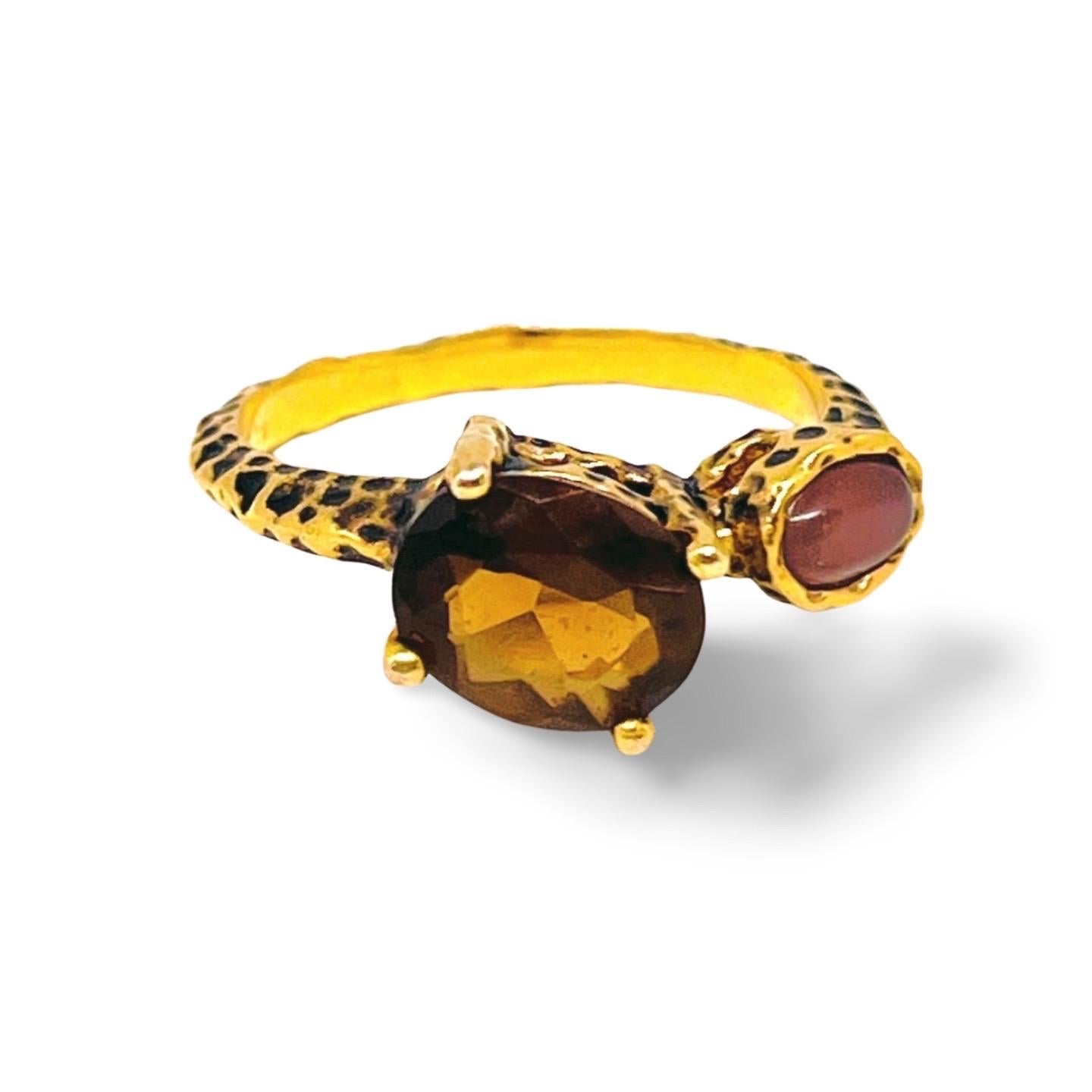 Cette bague artisanale en or 14k présente un design asymétrique saisissant avec une tourmaline brun-orange facettée et un cabochon d'œil de tigre teinté violet moyen. Cette bague faite à la main, à la texture martelée audacieuse et à la finition
