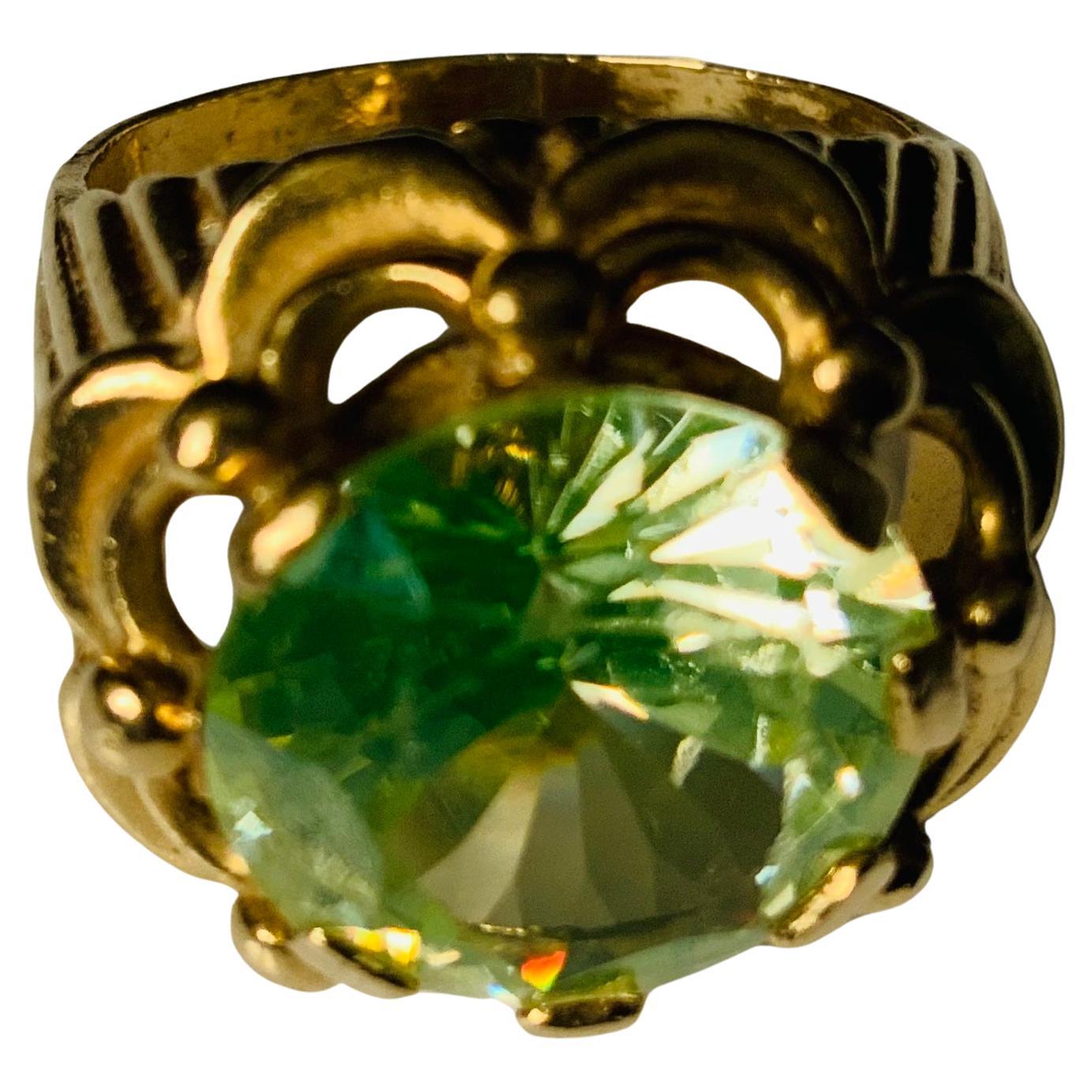 This a 14K yellow gold ring. It depicts a Brilliant Shape Zircon Beta type (12.11 x 7.17 mm ) weighing 8.15 carats  and mounted on seven gold prongs setting. Below the prong setting, the light green Zircon is adorned with a two levels swags enhanced