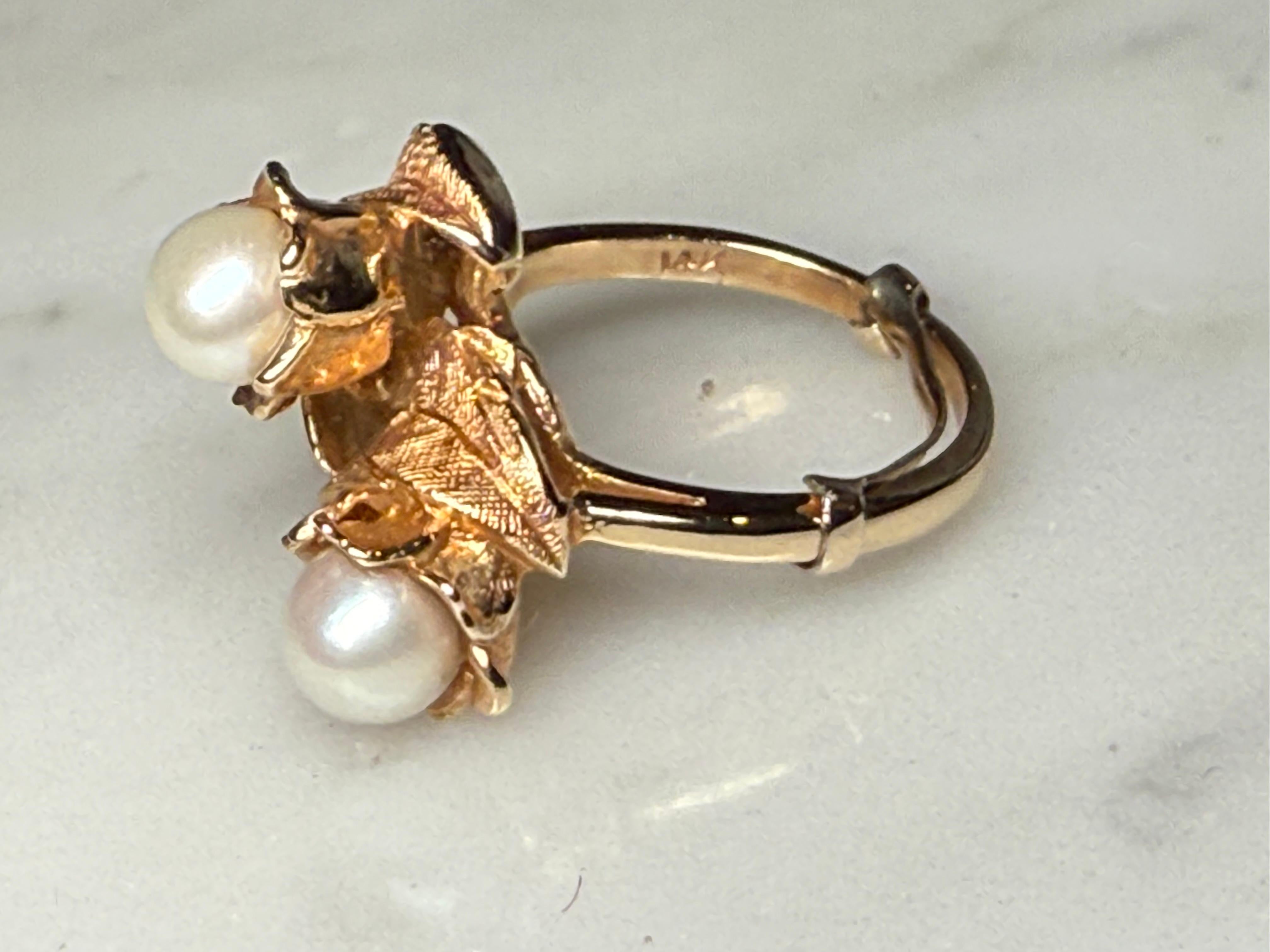 This is a 14K Yellow Gold Pearls Ring. It depicts a wrap around ring decorated with two flowers with leaves. Each flower is enhanced by a pearl attached to it. The ring is hallmarked 14k gold.