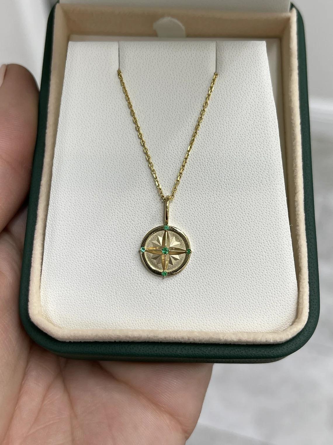 Un magnifique pendentif qui symbolise une boussole et ses directions. Chaque point (Nord, Ouest, Sud, Est) possède une délicate émeraude naturelle de taille ronde, avec une émeraude légèrement plus grande en plein milieu. Fabriqué avec soin en or 14