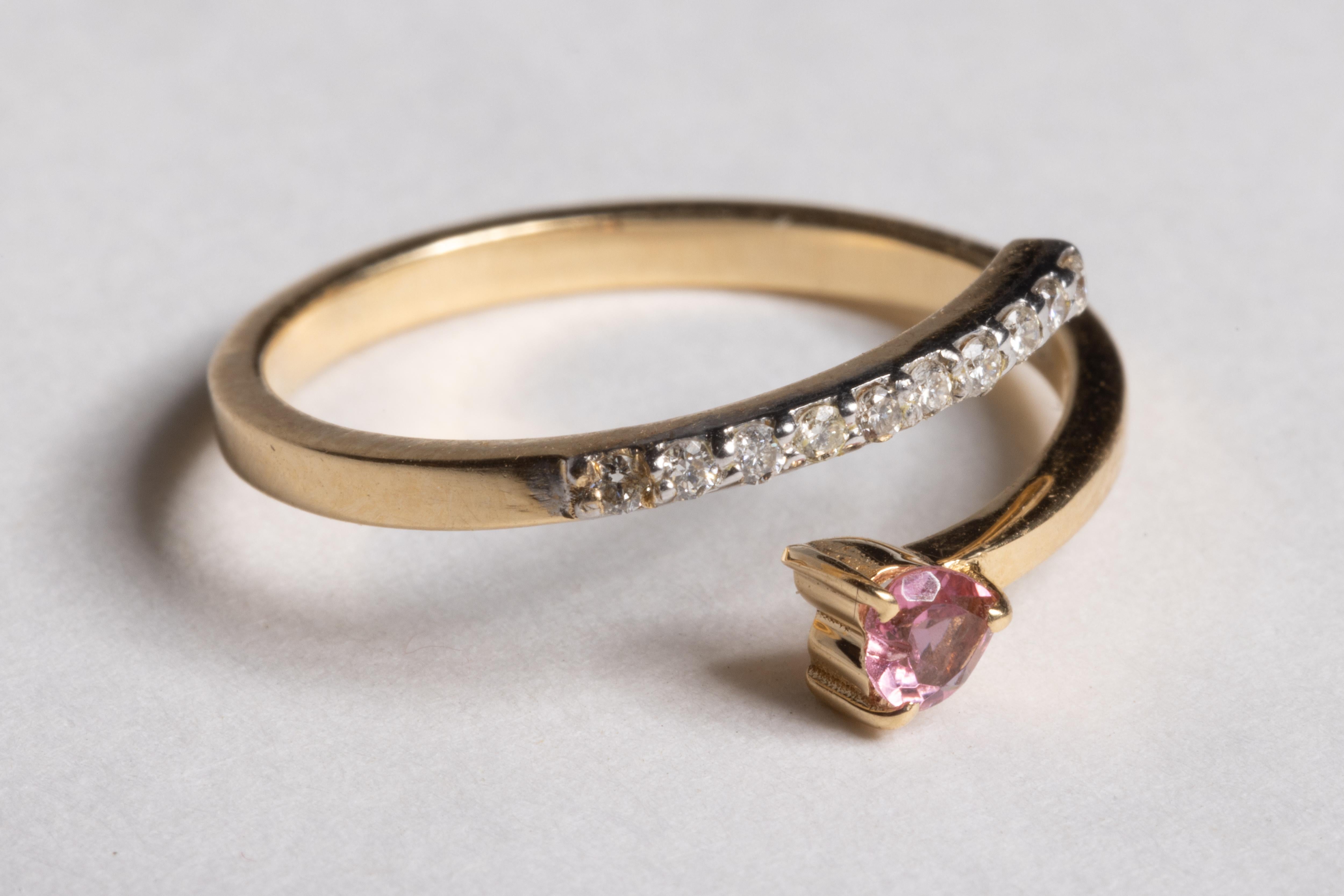 An unusual 14K gold overlapping coil ring with a heart-shaped, faceted pink sapphire and a row on top of the band of round, brilliant cut diamonds.  Can be adjusted.  Carat weight of the pink sapphire is ,11 carats, the diamonds total .98 carats. 