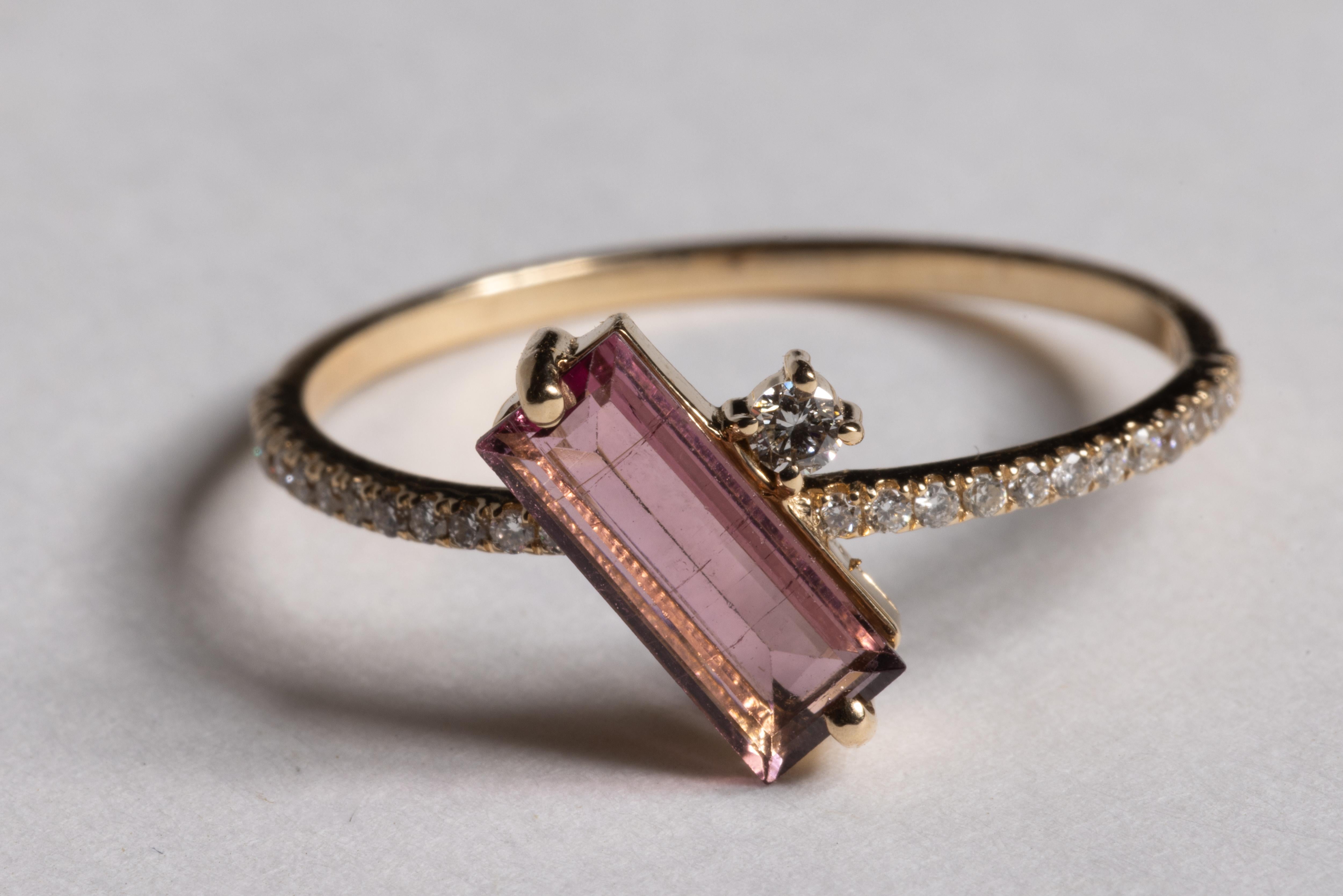 Un insolito anello in oro 14K con una gemma di tormalina rosa taglio smeraldo al centro e un diamante rotondo taglio brillante accanto.  Gli stessi diamanti taglio brillante adornano la parte superiore della fascia.  La tormalina rosa è di 0,74