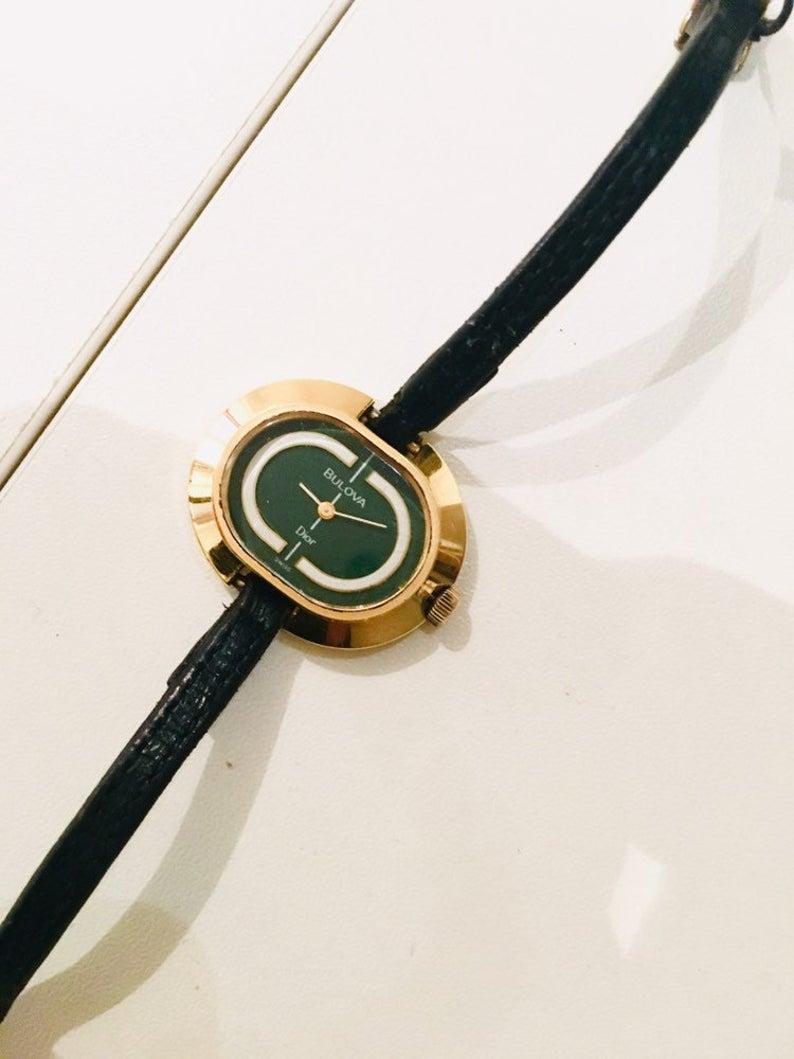 14K gold plated Dior by Bulova wrist wind up watch, fully working, green and white face, original black leather strap

Condition: Early 1970s, gold metal ware is in very good condition, watch face has some light scratches but no cracks, original