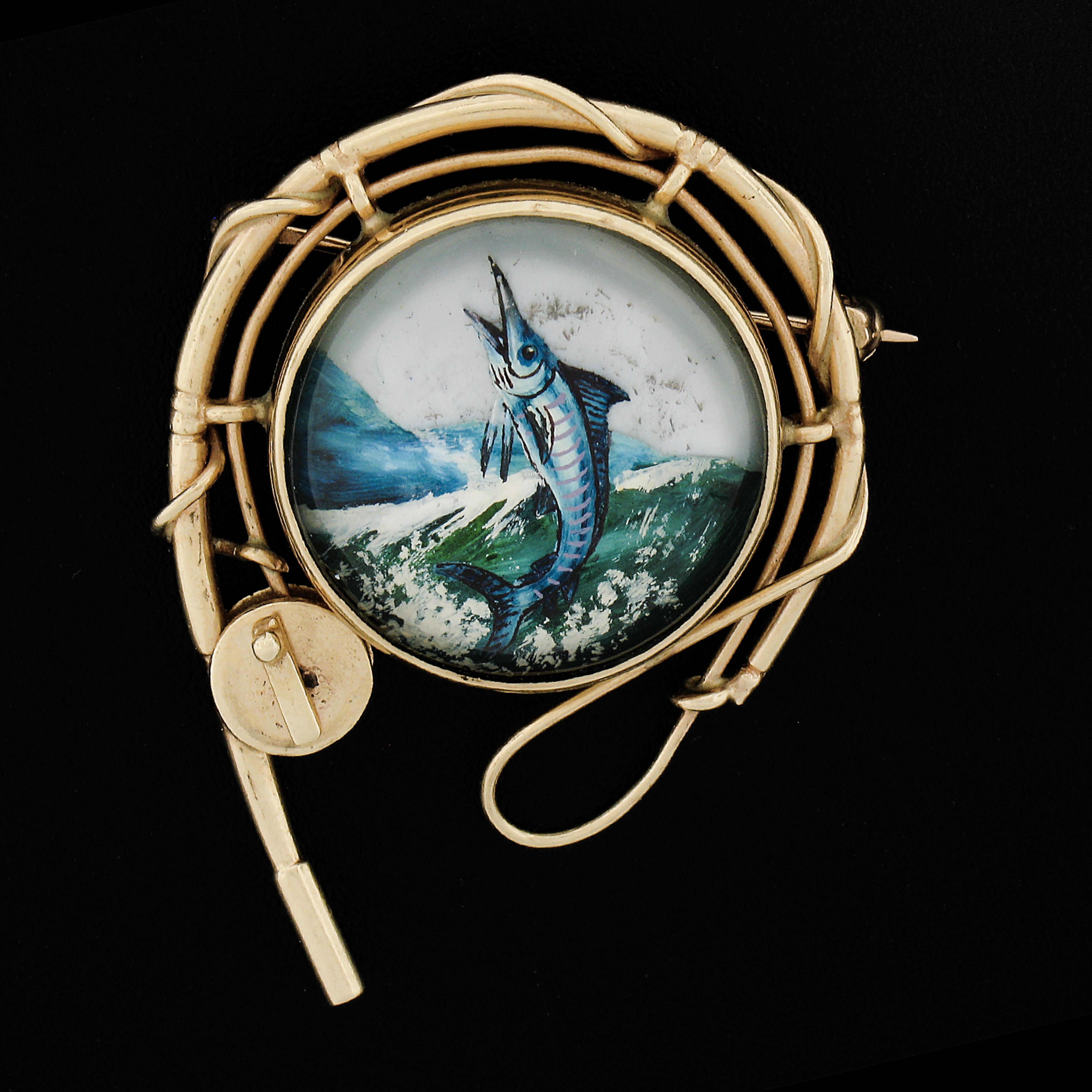 This magnificent vintage brooch was crafted from solid 14k yellow gold. It features an incredibly detailed reverse painted intaglio of a marlin fish jumping of the ocean. This brooch displays outstandingly detailed work and looks incredible and it