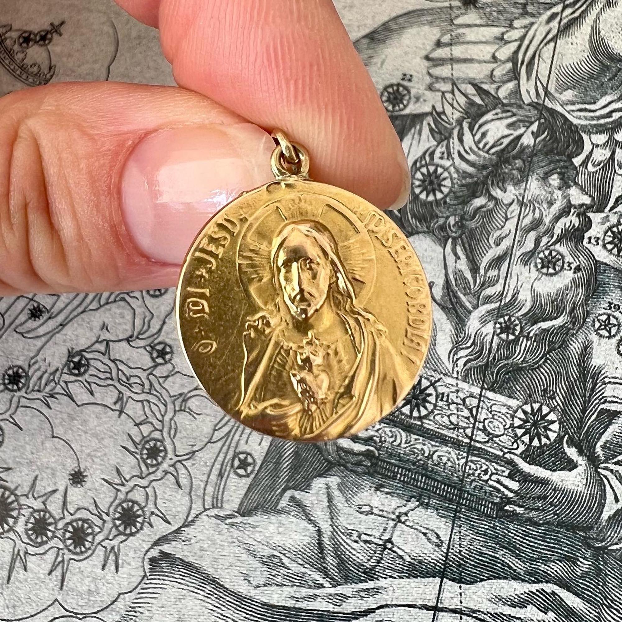 A round religious sacred heart gold medal charm pendant. On one side the medal bears the image of Christ surrounded by the inscription: O mi Jesu Misericordia! On the other side Madonna with her child, enthroned on a cloud surrounded by angelic