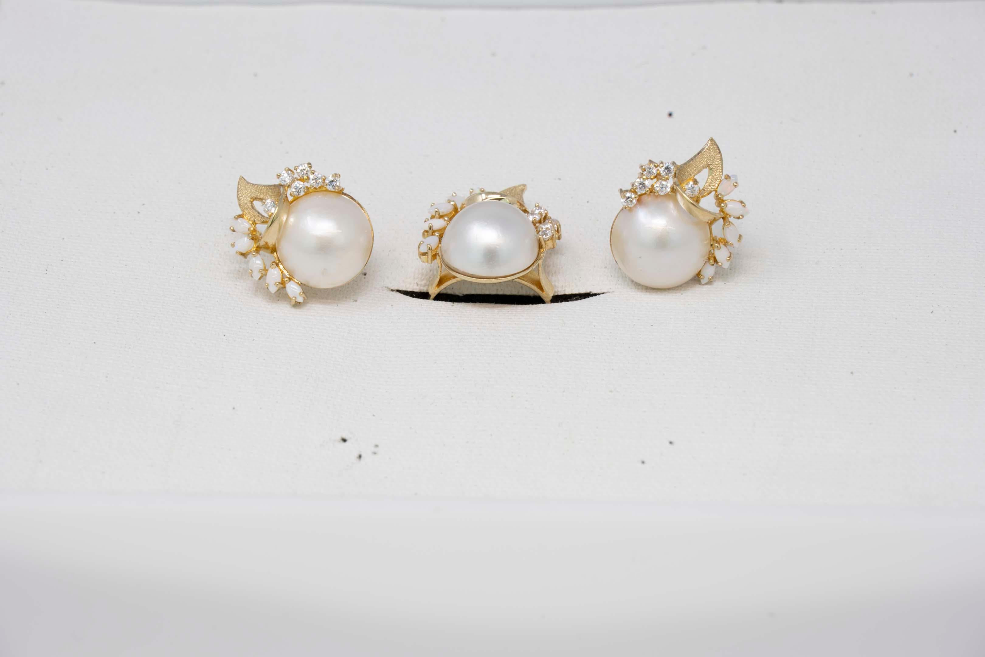 14k yellow gold set of ladies ring & earrings with 14mm Mabe pearl, 6 diamonds each and 5 opal gemstones each. Ring is size 7.75. The earrings has the omega clip, stamped 14k GA. In good condition.
