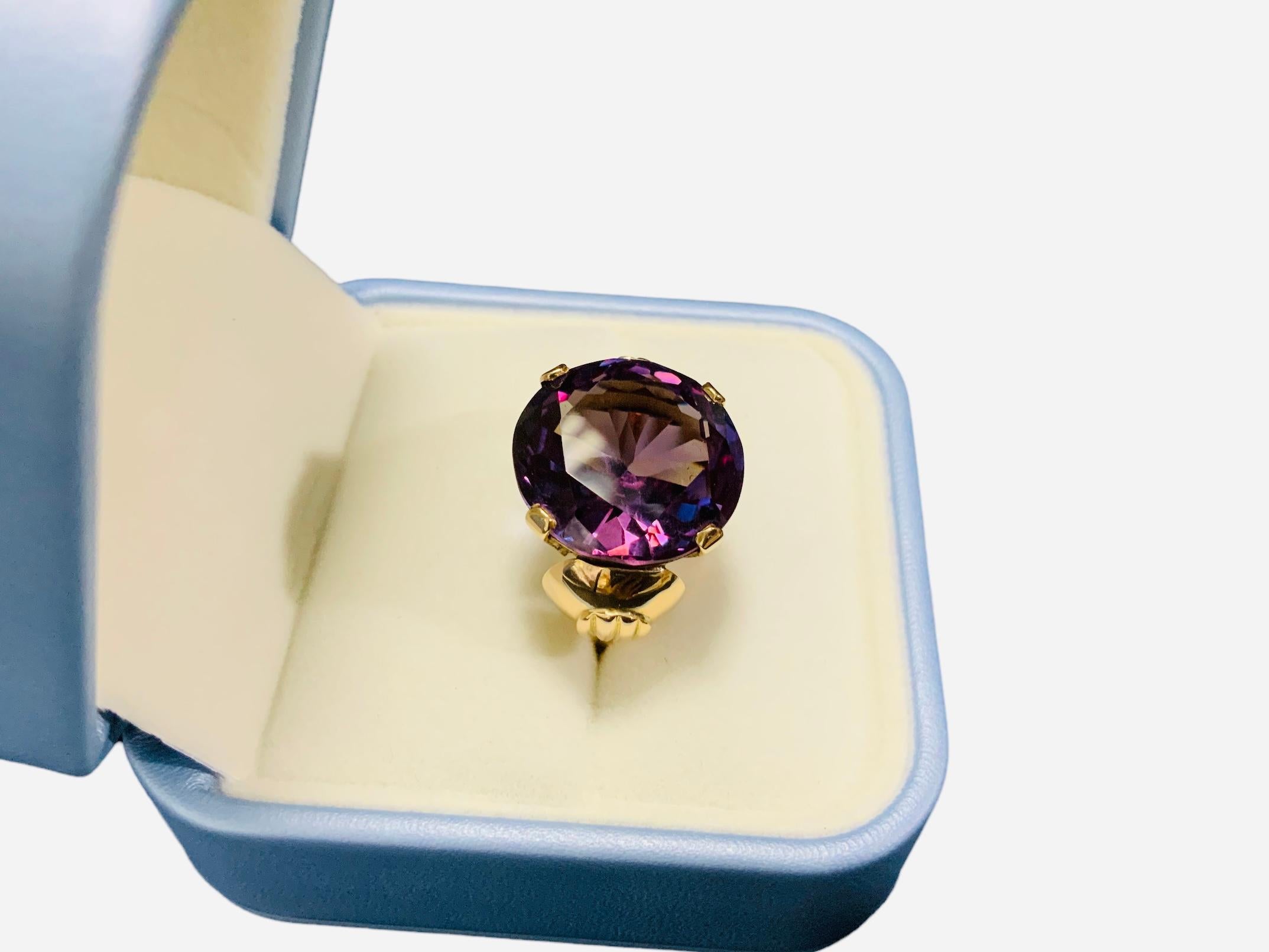 This a 14K yellow gold lab created Alexandrite ring. It depicts a  large round faceted purple color Alexandrite stone mounted  on four gold prongs setting. The front and back walls of the gallery are decorated with hearts shaped by scrolls. The side