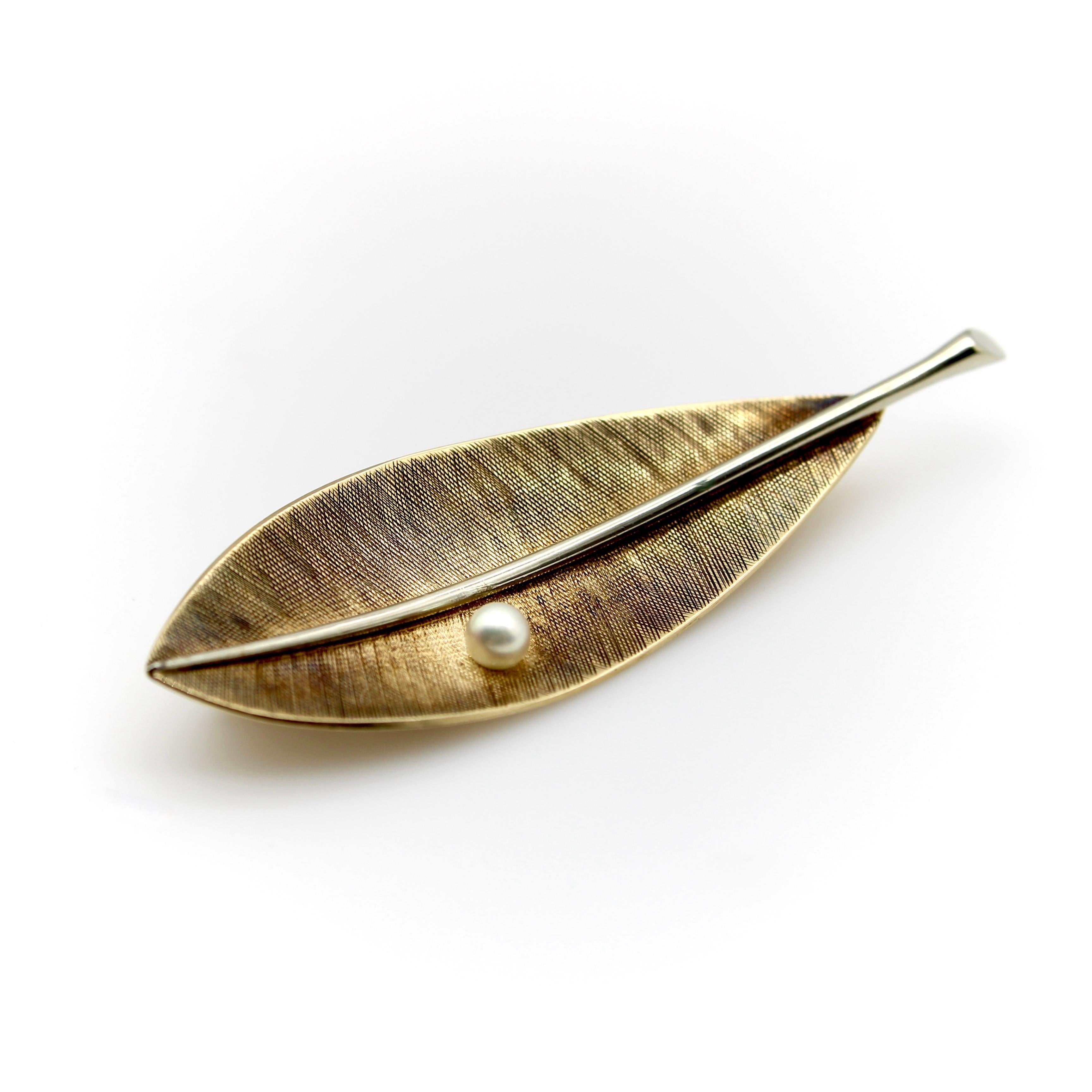 Elegant and simplistic in design, this leaf in yellow and white 14k gold is a classic Tiffany & Co. piece. A pearl sits on the crosshatched gold, looking like a drop of dew. Down the center of the leaf is the use of white gold as a stem that creates