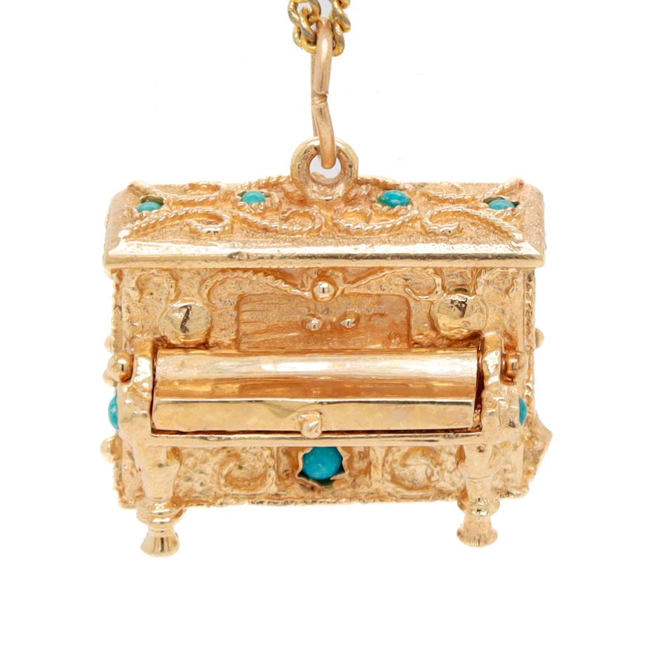 A very fine figural gold piano charm.

In 14k gold. 

With a heavy, cast body and a hinged cover that reveals articulated piano keys, bezel-set turquoise cabochons, and applied rope and granulation details throughout.

Set with a bail to the top
