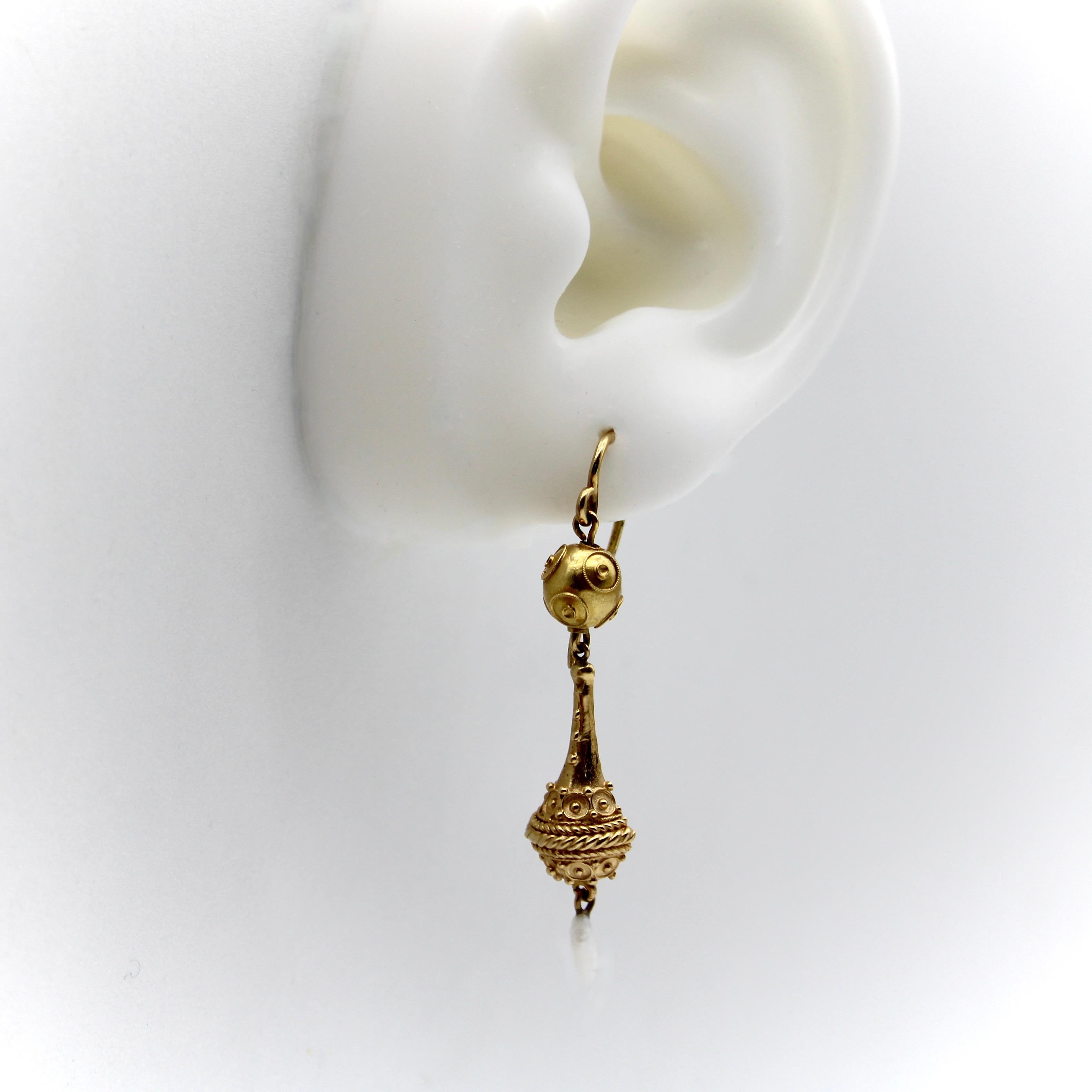 This is a stunning pair of 14k Etruscan Revival drop earrings featuring intricate gold detailing and a delicate Mississippi river pearl dangling element. The shape of the earrings resembles an elongated urn hanging from an Etruscan Revival ball.