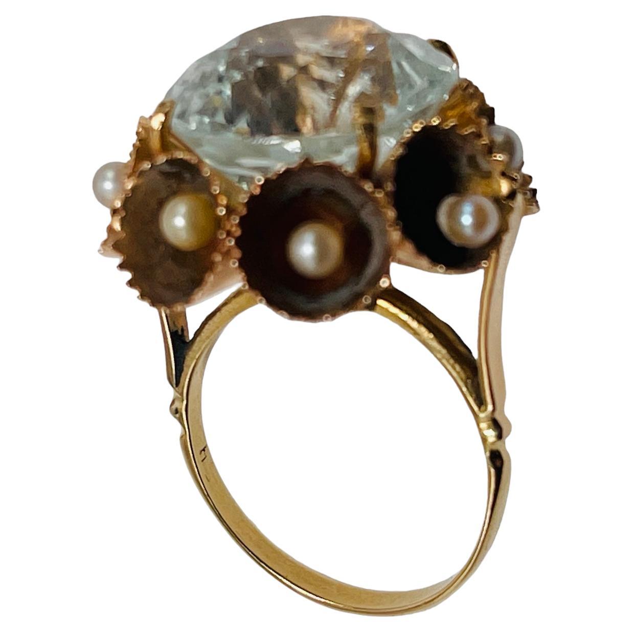 This a 14K yellow gold ring. It depicts a Brilliant Shape White Sapphire (15.18 x 15.18 x 9.73 mm ) weighing 16.14 carats and mounted on four gold prongs setting. The White Sapphire is adorned around it with a wreath made of gold trumpets with