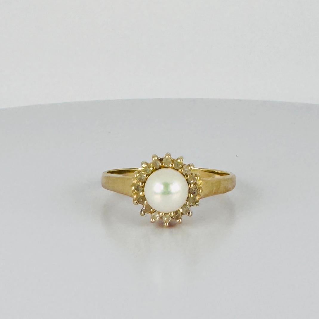 A captivating vintage treasure that radiates elegance and refinement. This golden entourage ring features a luminous round pearl, encircled by a subtle sparkle of tiny diamonds – a timeless design that effortlessly complements any