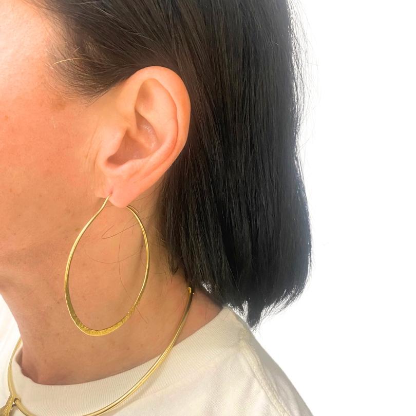 A pair of 14k hammered gold flat hoop earrings.
The hoops feature a sleek profile, giving them a contemporary look. The hammered texture adds
a subtle, organic pattern. These hoop earrings catch light beautifully and have a graceful,