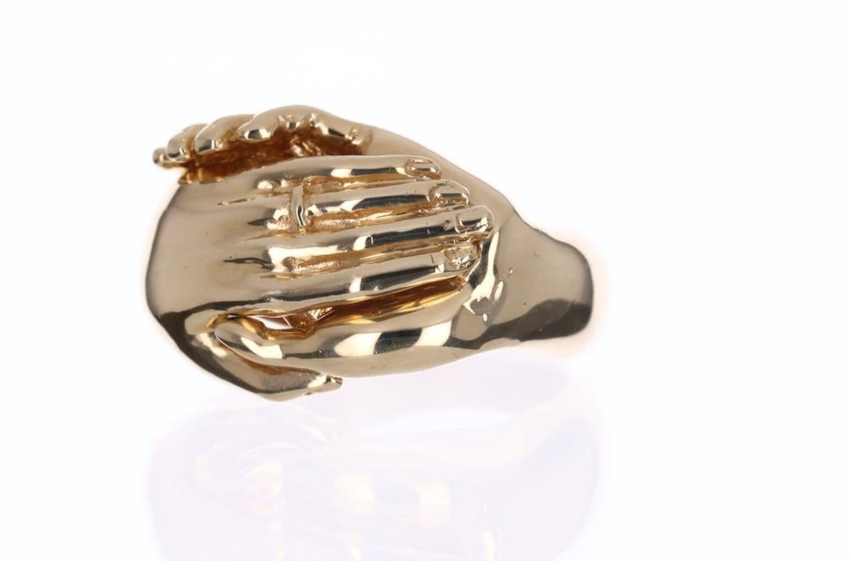A vintage 14K gold puzzle ring with two hands holding a heart inside that is engraved 