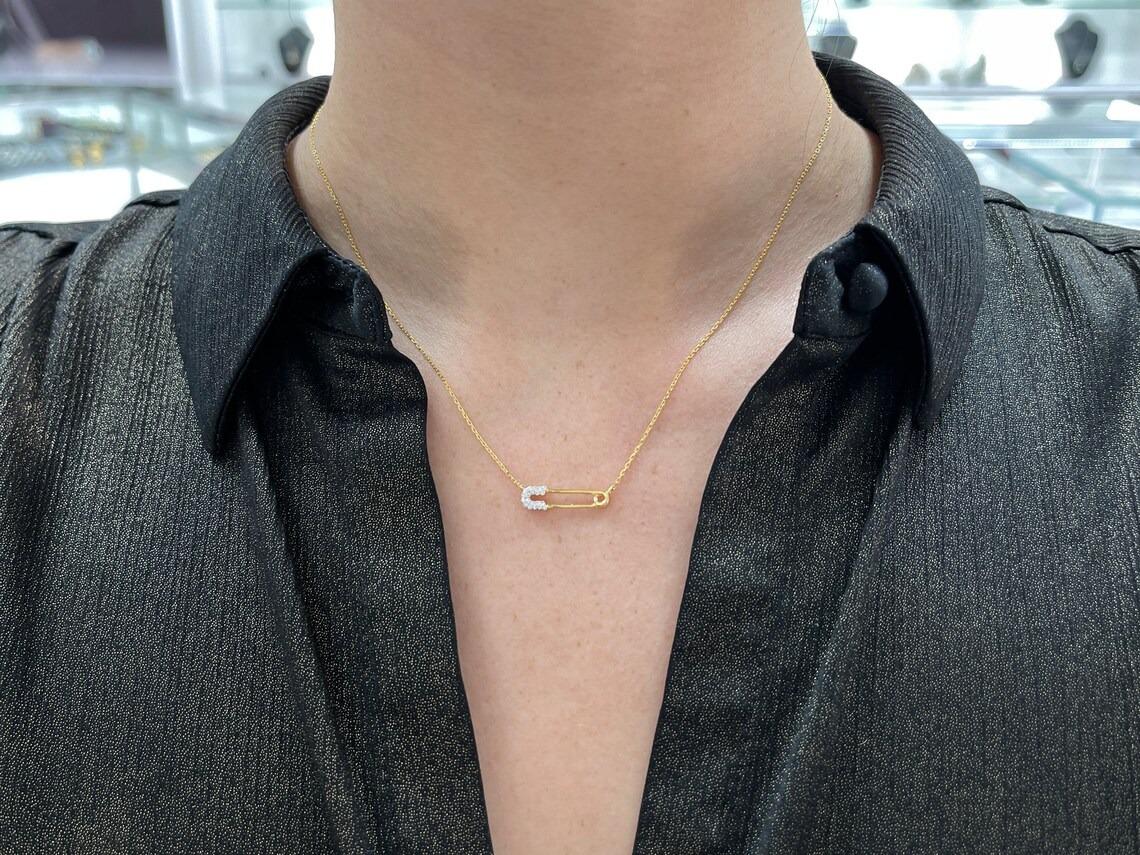 Featured is a stunning natural diamond safety pin gold necklace. This piece features a lovely safety pin with diamond accents over the base, attached to an adjustable 16-18 inch cable chain. Crafted in 14K gold, in the color of your choice. Perfect