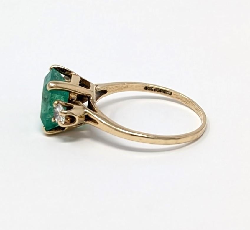 Bague vintage en or jaune massif 14k à trois pierres, mettant en vedette une émeraude naturelle vibrante au centre, accentuée par un diamant de chaque côté. Signé 14K JTC 969 sur l'intérieur de la bande, meilleure mesure pour un doigt de taille US