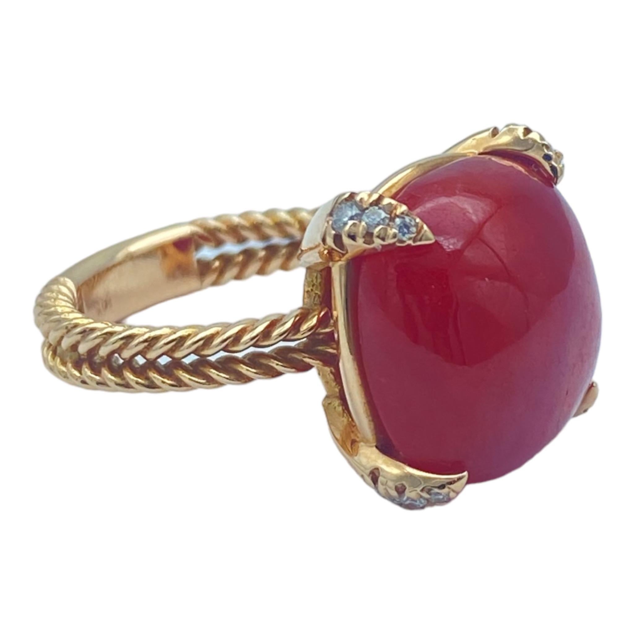 The Red Coral sugarloaf and diamond ring is set in a 14-karat pink or rose gold ring. The ring is a rope-textured style with diamond prongs holding the center stone. The Coral is a sugarloaf cushion cut measuring 14.10 mm in diameter. The diamonds
