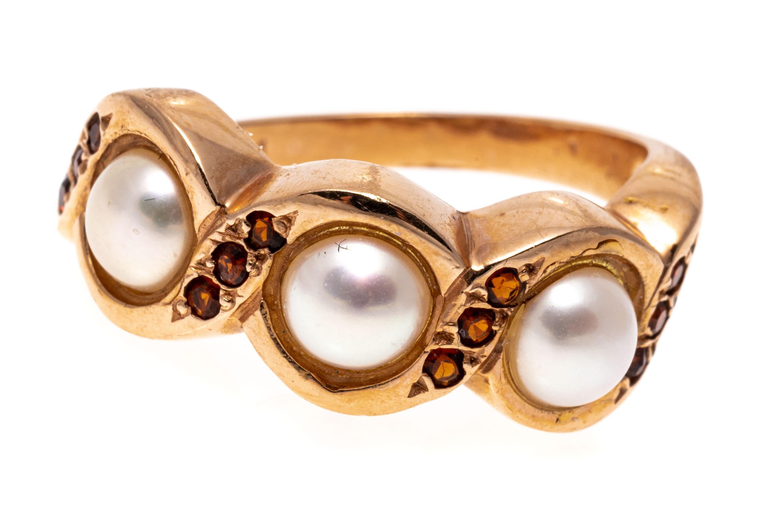 14K rose gold ring. This lovely ring is a swirling band set with three white cultured freshwater pearls, decorated with round faceted, accent garnets, approximately 0.12 TCW.
Marks: 14K
Dimensions: 13/16