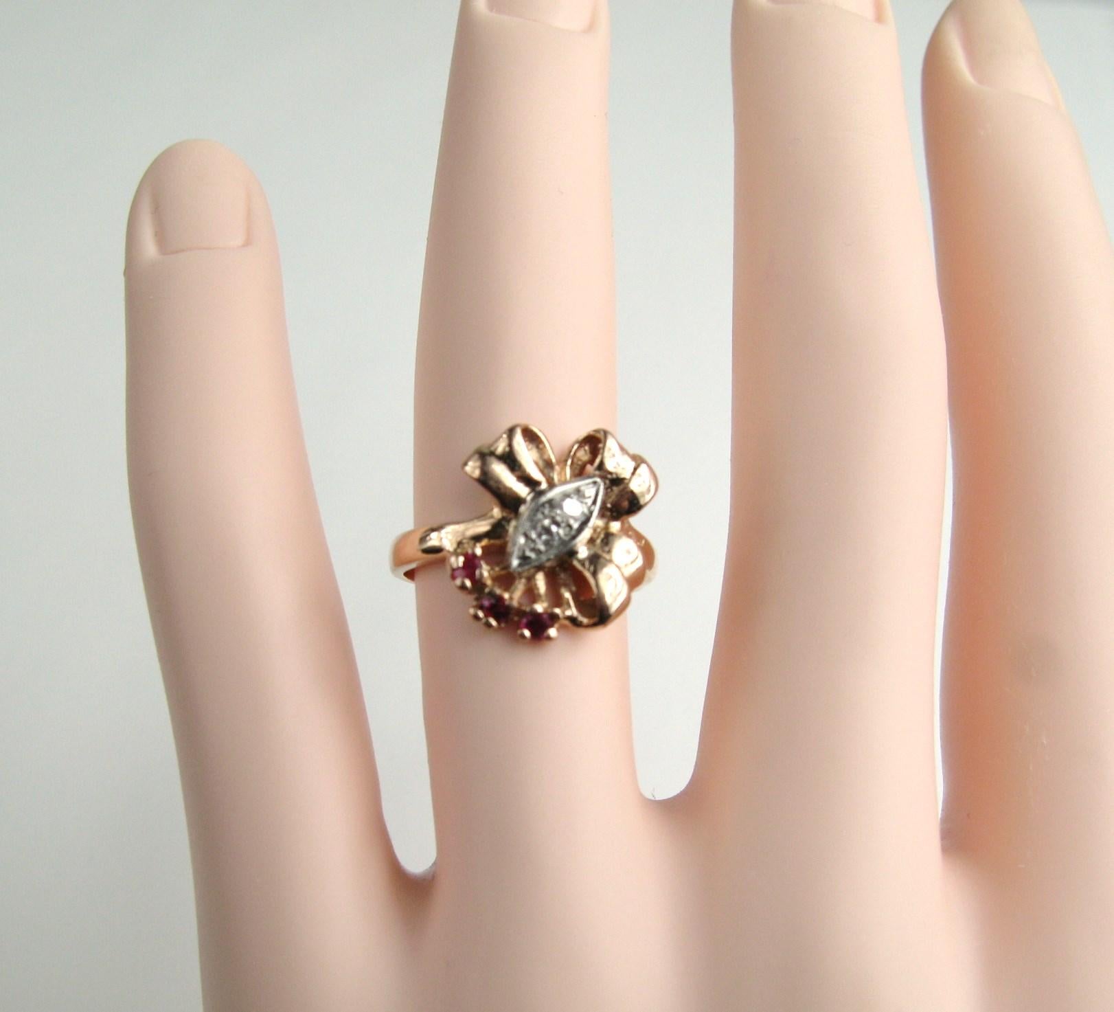Delicate as a spring flower, this ring features prong set rubies and tiny accent diamonds set in 14K Rose Gold. The ring is a size 6.5 and can be sized by us or your jeweler. Measuring .57in. x .53in. This is out of a massive collection of