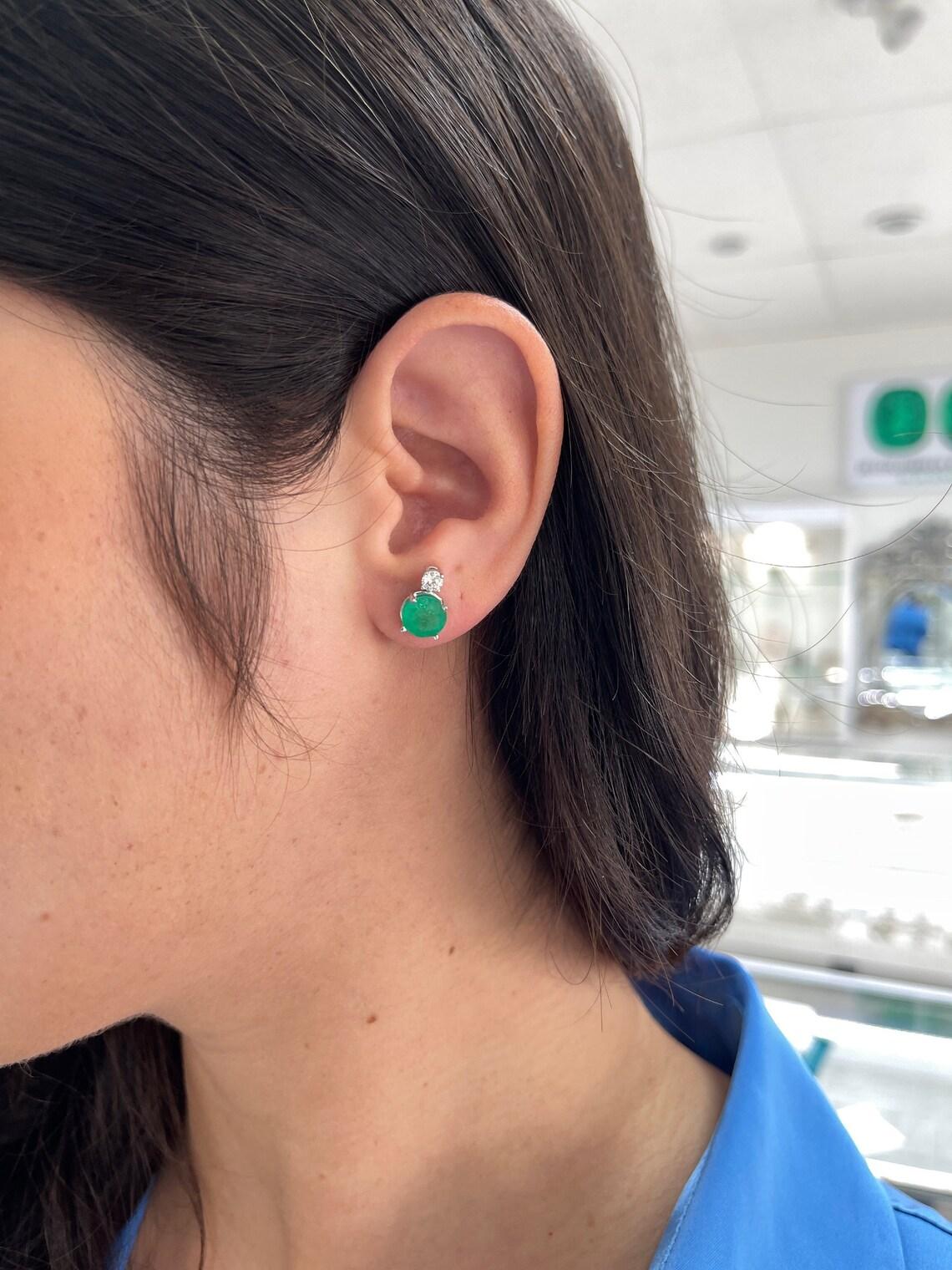 Indulge in the enchanting beauty of our Emerald and Diamond Stud Earrings, a masterpiece that captures the essence of luxury. Showcasing 3.15 carats of natural round-cut Colombian emeralds, radiating a vivacious rich dark green hue, these gems come