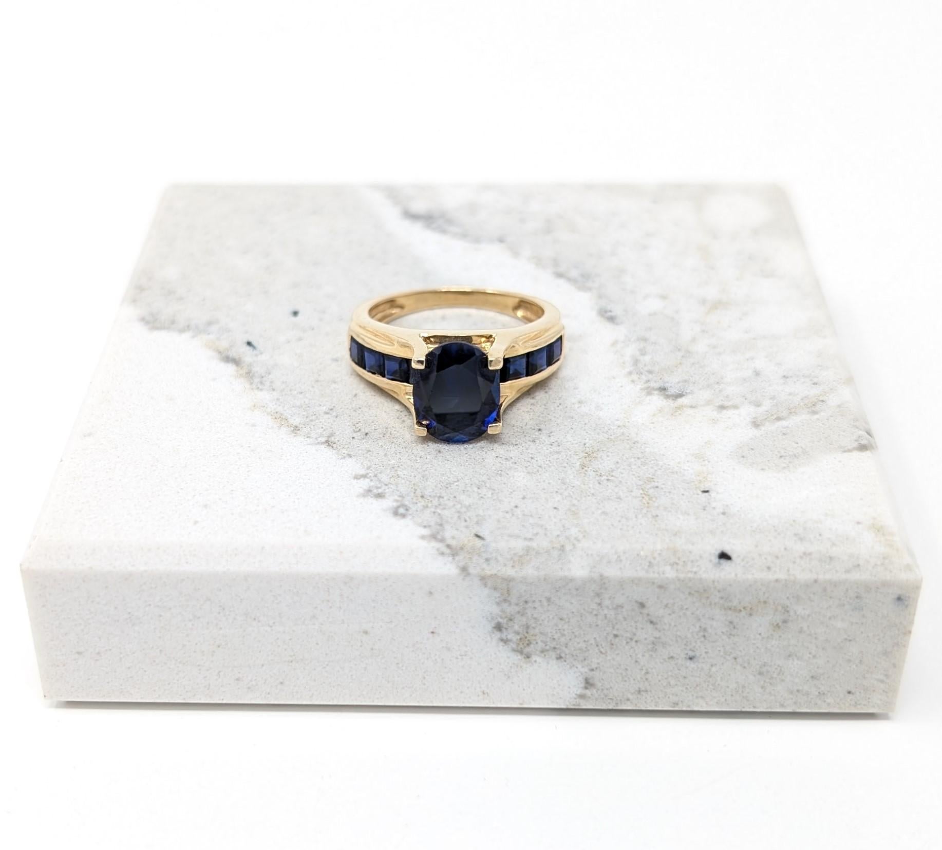 A stunning 14k solid yellow gold ring showcasing a rich intense oval cut royal blue sapphire centerpiece accented by channel set sapphires. Hallmarked on the interior of the ring 14K along with an unknown makers mark. Best fits for a US size 7