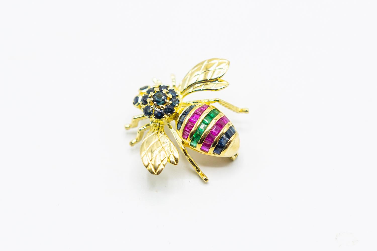 14K yellow gold brooch featuring 0.50 carats of square step cut and round modified-brilliant sapphires, 0.50 carats of square step cut rubies and 0.30 carats of square step-cut emeralds with pin closure.