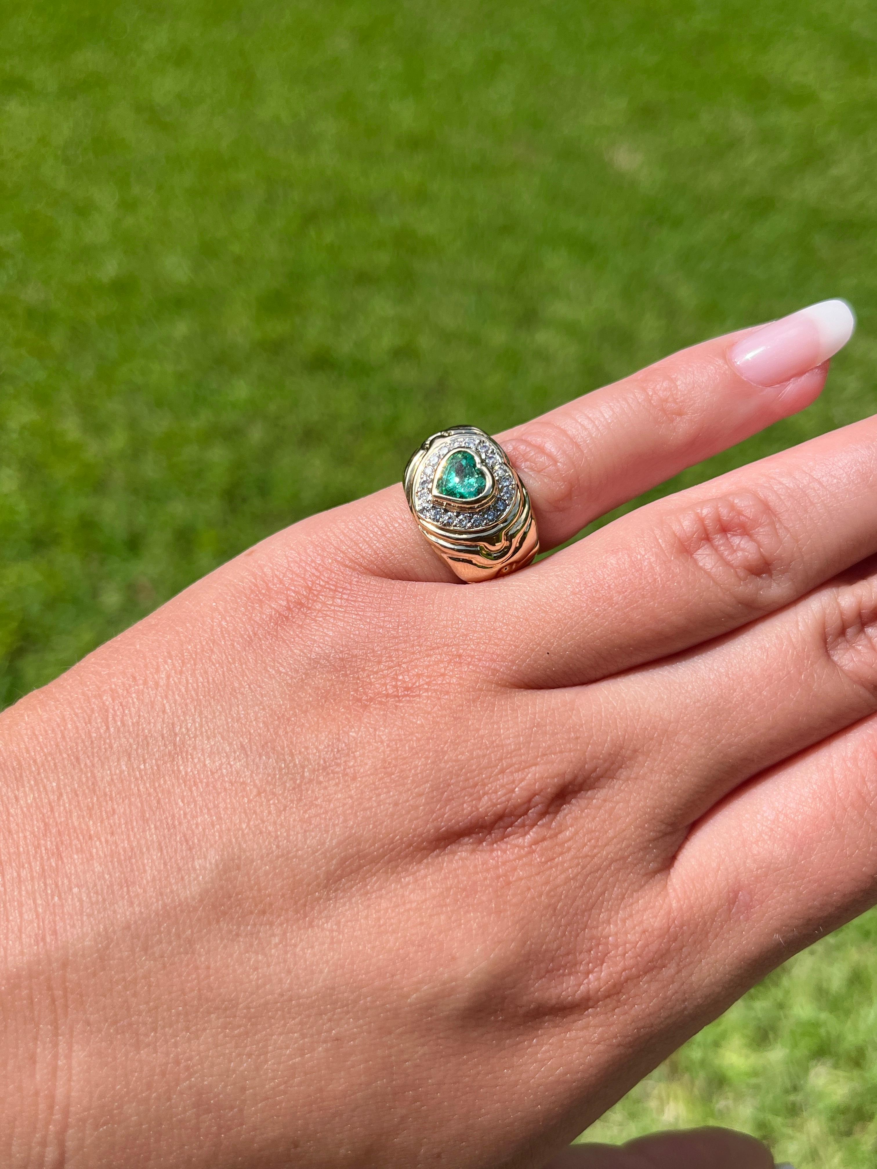 Heart cut natural emerald and round cut diamond ring in 14k solid gold. Set in a wide face heart motif bezel setting and textured ring shank. This wide shank ring is a 13mm width that provides excellent coverage on the finger. Textured ring shank