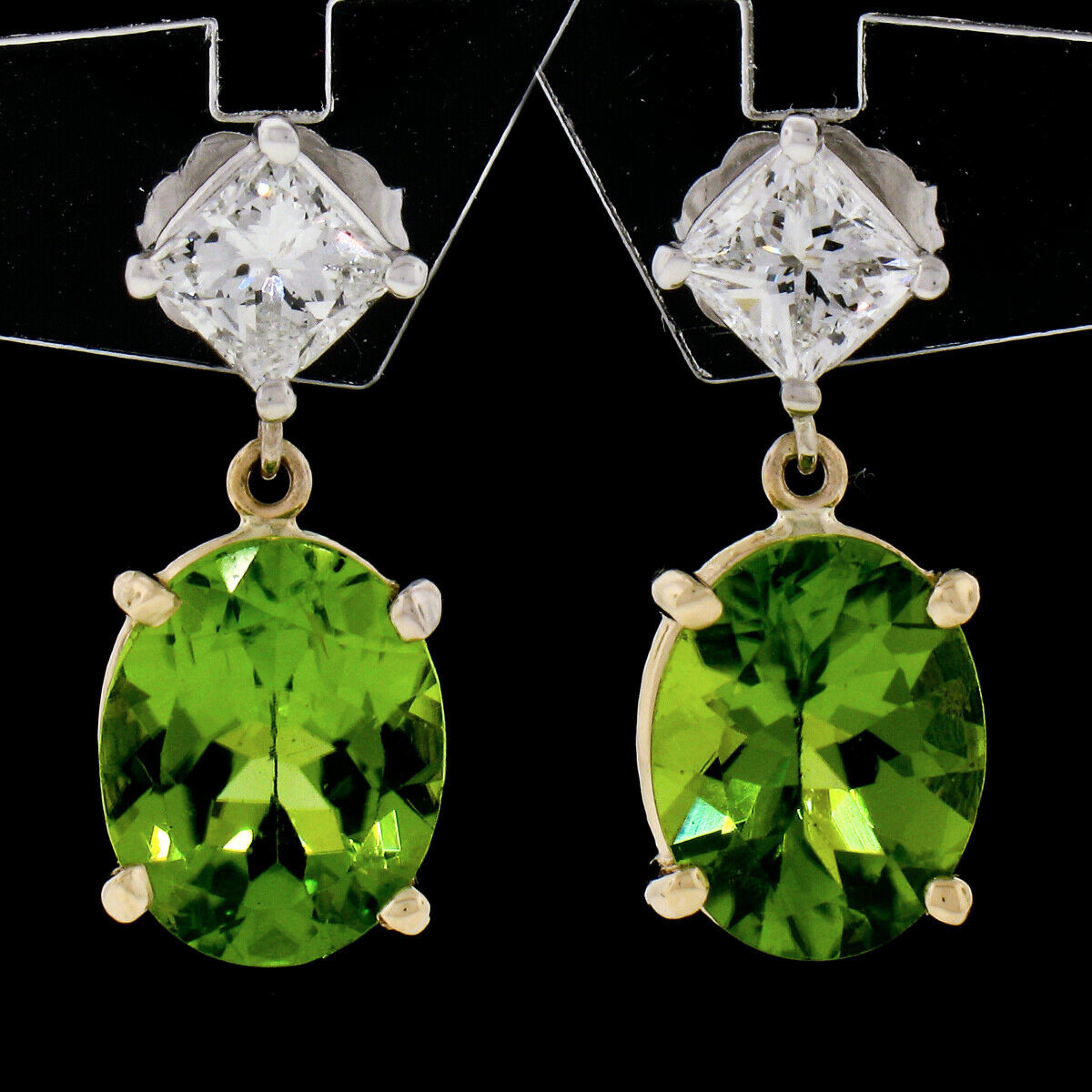 These fancy peridot and diamond drop/dangle earrings are crafted in solid 14k yellow and white gold and feature very well made prong settings that each elegantly embraces a gorgeous stone at its center. The beautiful, princess cut diamonds show