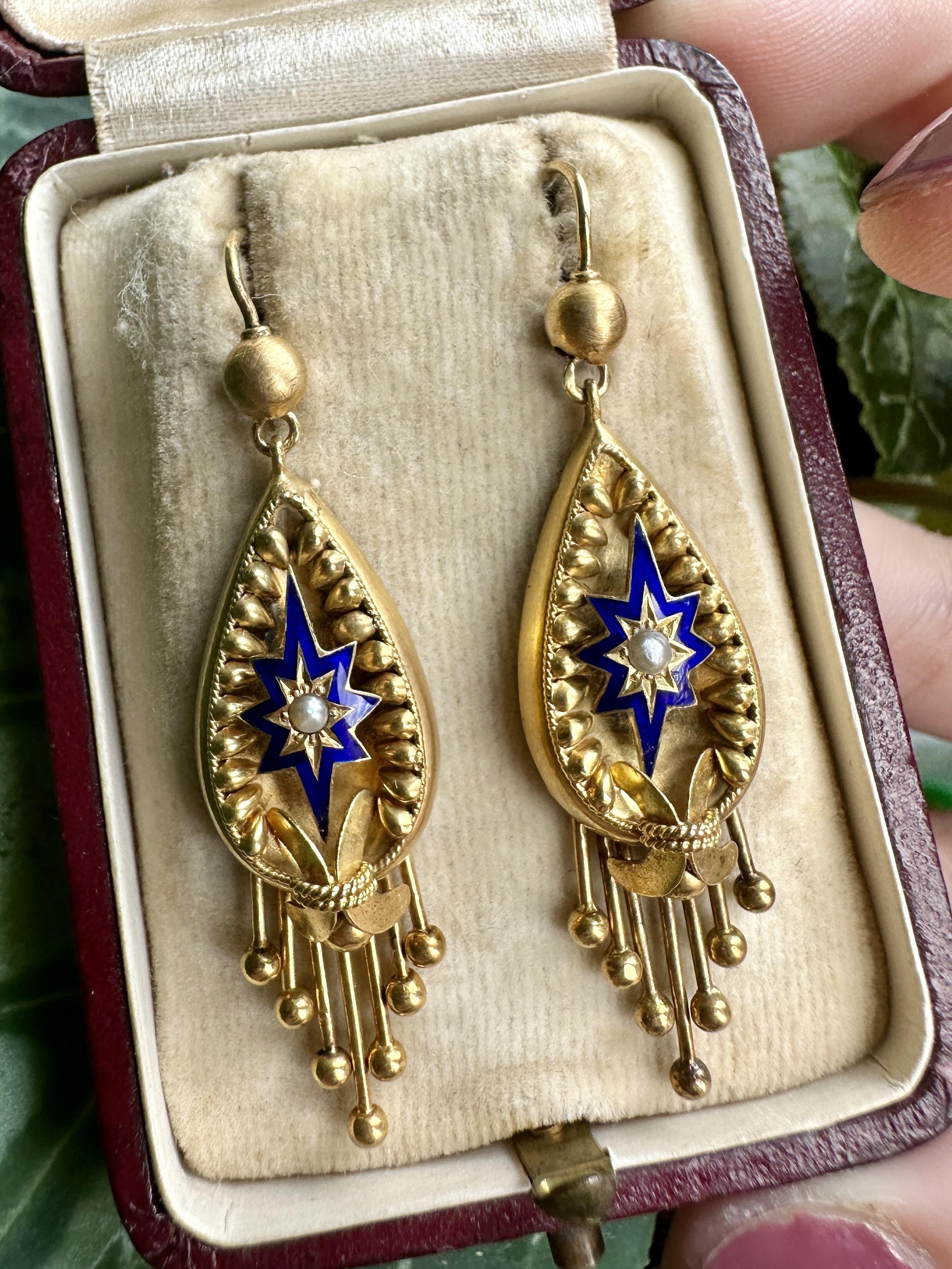 Elevate your elegance with these exquisite 14k Victorian Pearl and Blue Enamel Drop Earrings. Crafted from luxurious yellow gold, these 2 inch earrings feature beautiful pearls in the center and blue enamel designs surrounding it. In good condition