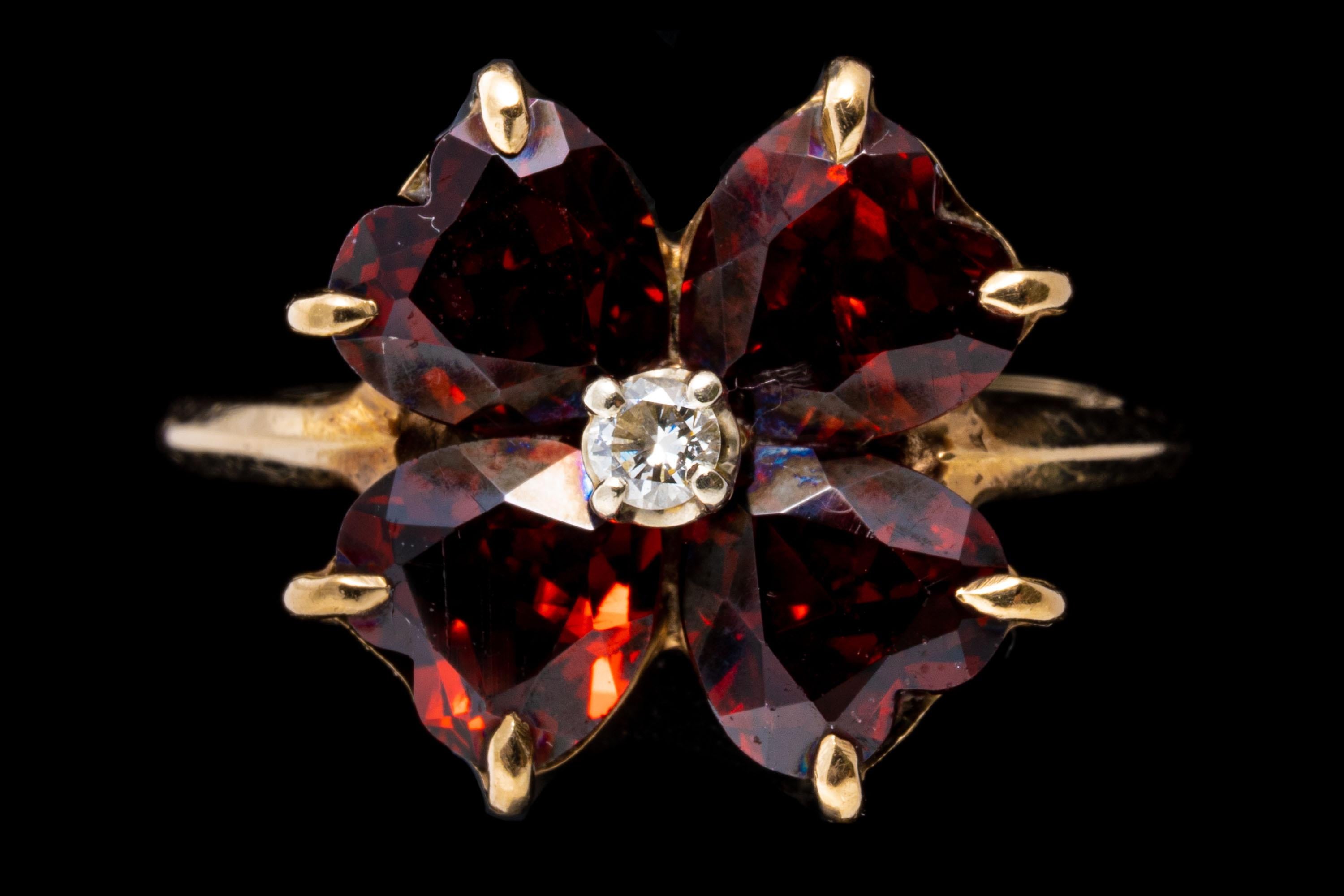 This pretty yellow gold vintage ring is a clover motif, decorated with four faceted, heart-shaped burgundy color almandine garnets, approximately 2.56 TCW, centering a round faceted diamond, approximately 0.04 CTS. All of the stones are prong