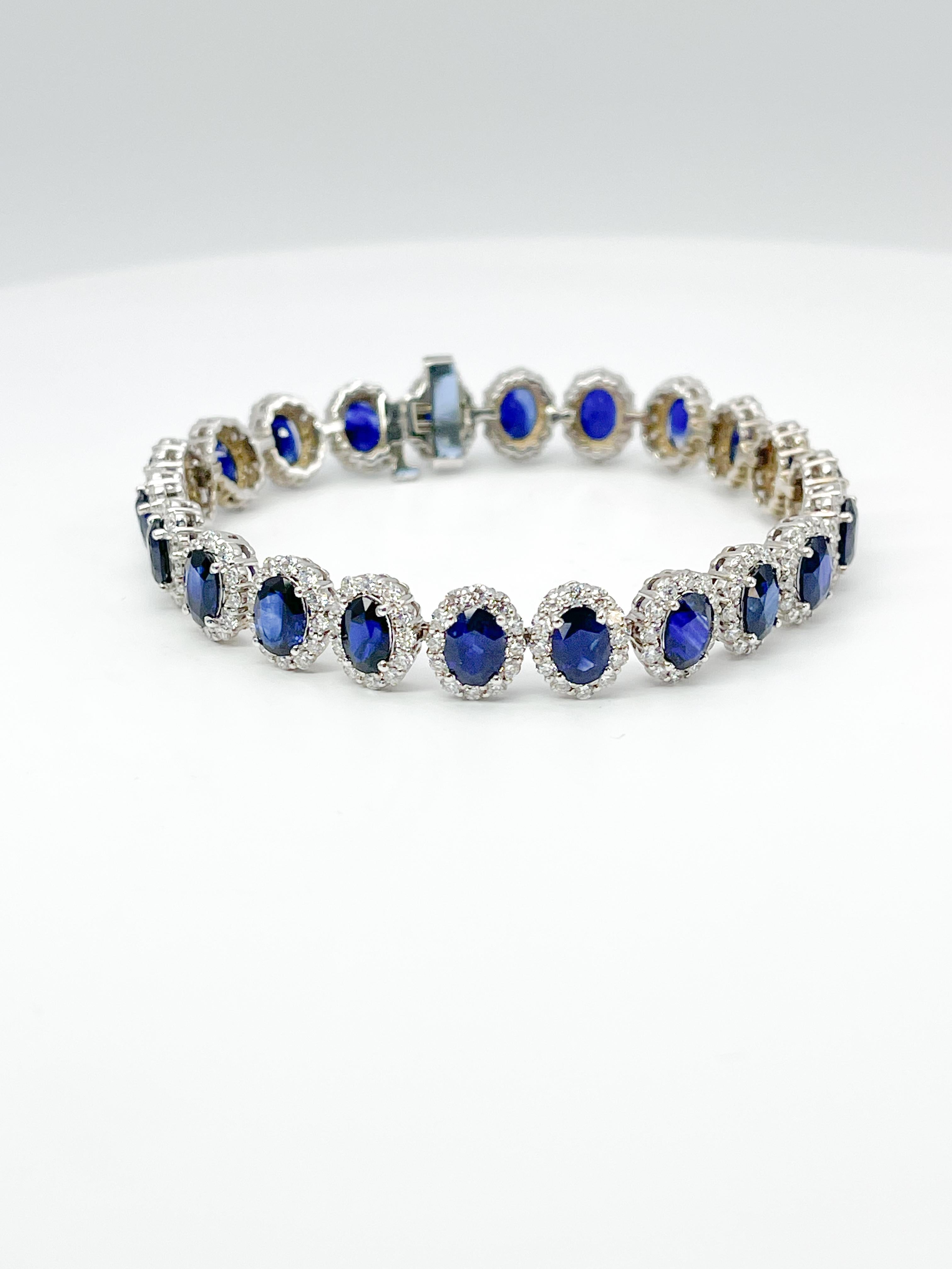 This beautiful 14k white gold tennis bracelet has 22 beautiful blue sapphires 22ct tw AA quality in it along with a diamond halo around each stone. The Diamonds are 7ct tw VS2 G. The bracelet has a tongue clasp with an under safety bracket, the full