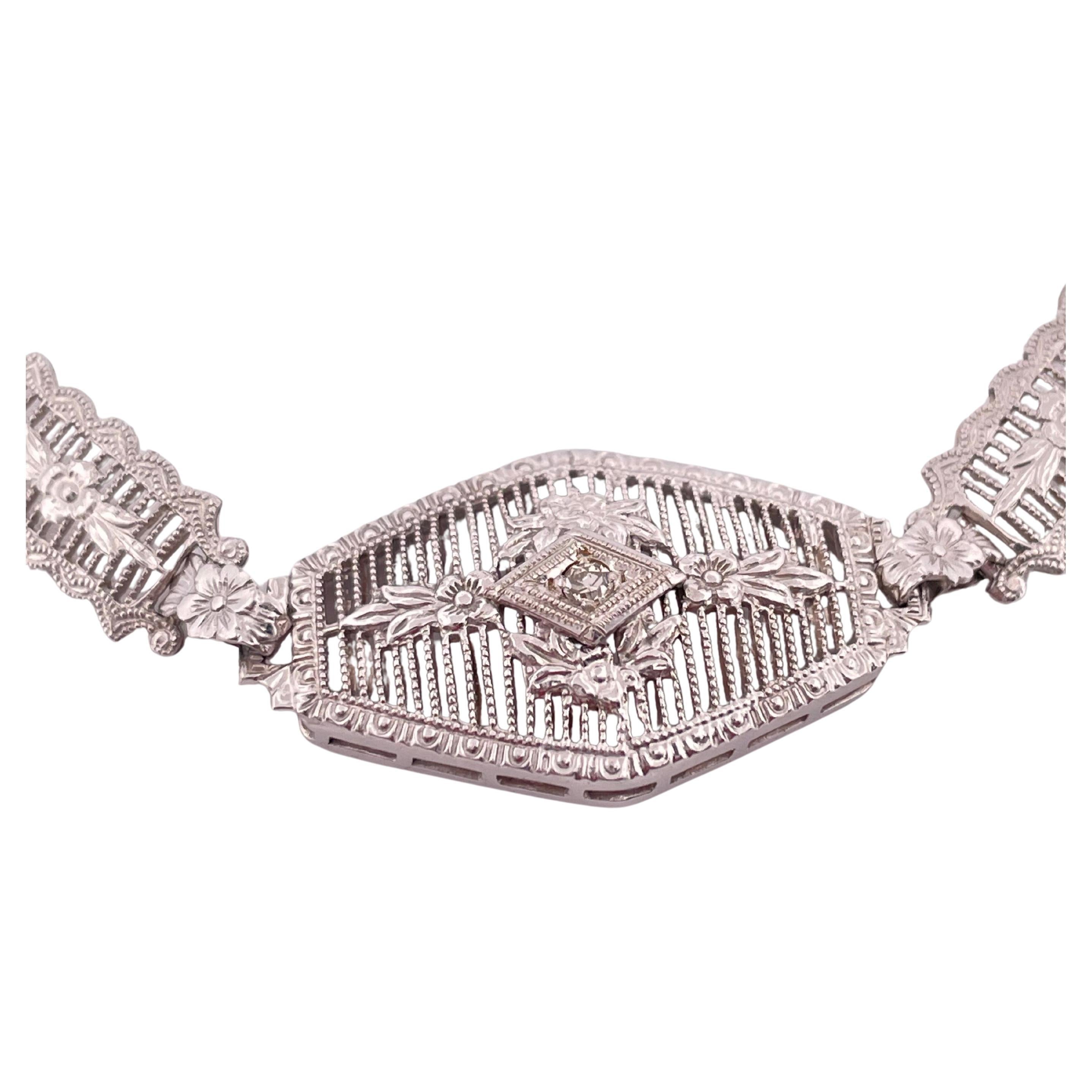 Esta exquisita pulsera de oro blanco de 14 quilates muestra la refinada artesanía de la época Art Déco. Con un intrincado diseño de filigrana, la pulsera está adornada con un delicado diamante de 0,10 quilates de peso total engastado en el centro de