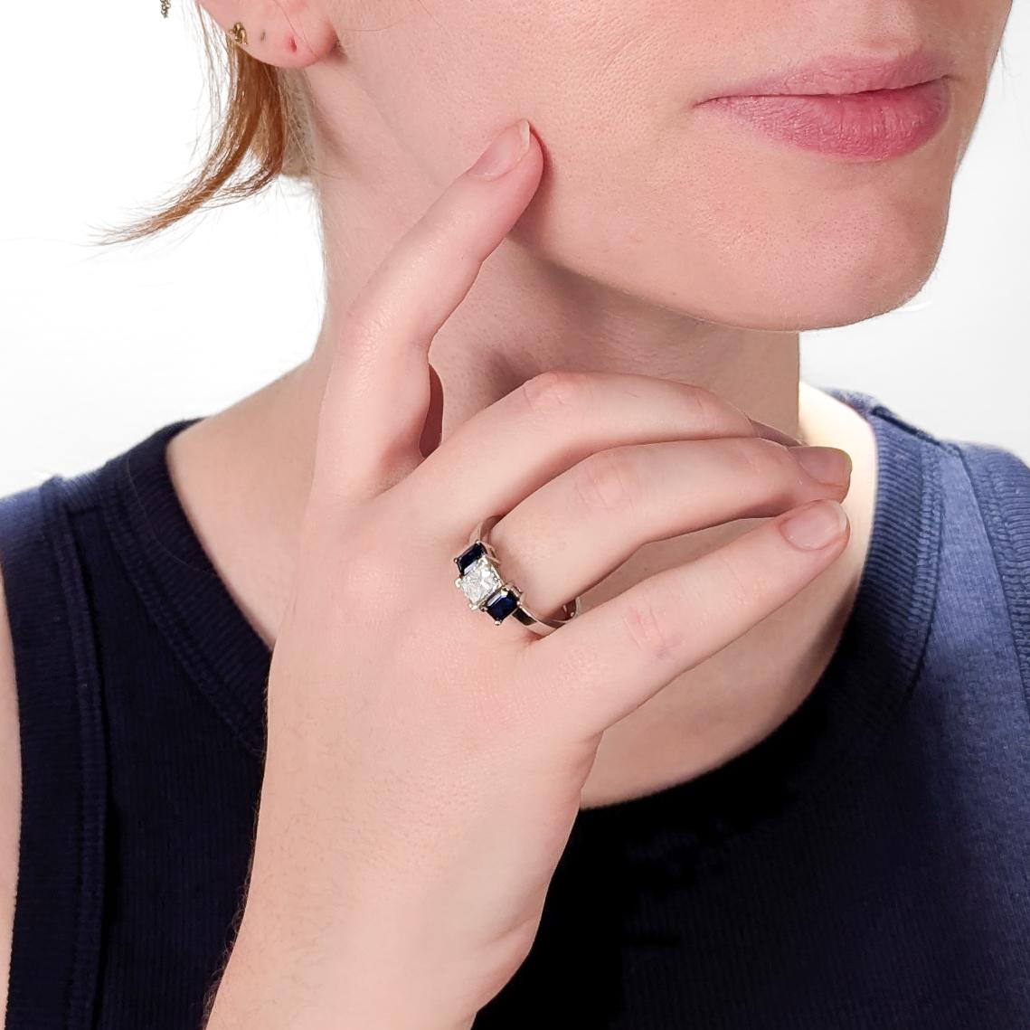 Bague de fiançailles à trois pierres en or blanc, diamants et saphirs.

En or blanc 14 carats.

Avec un diamant central de 1,20± ct. de taille radiant serti en panier, flanqué de deux saphirs bleus de taille émeraude.

Marqué sur la