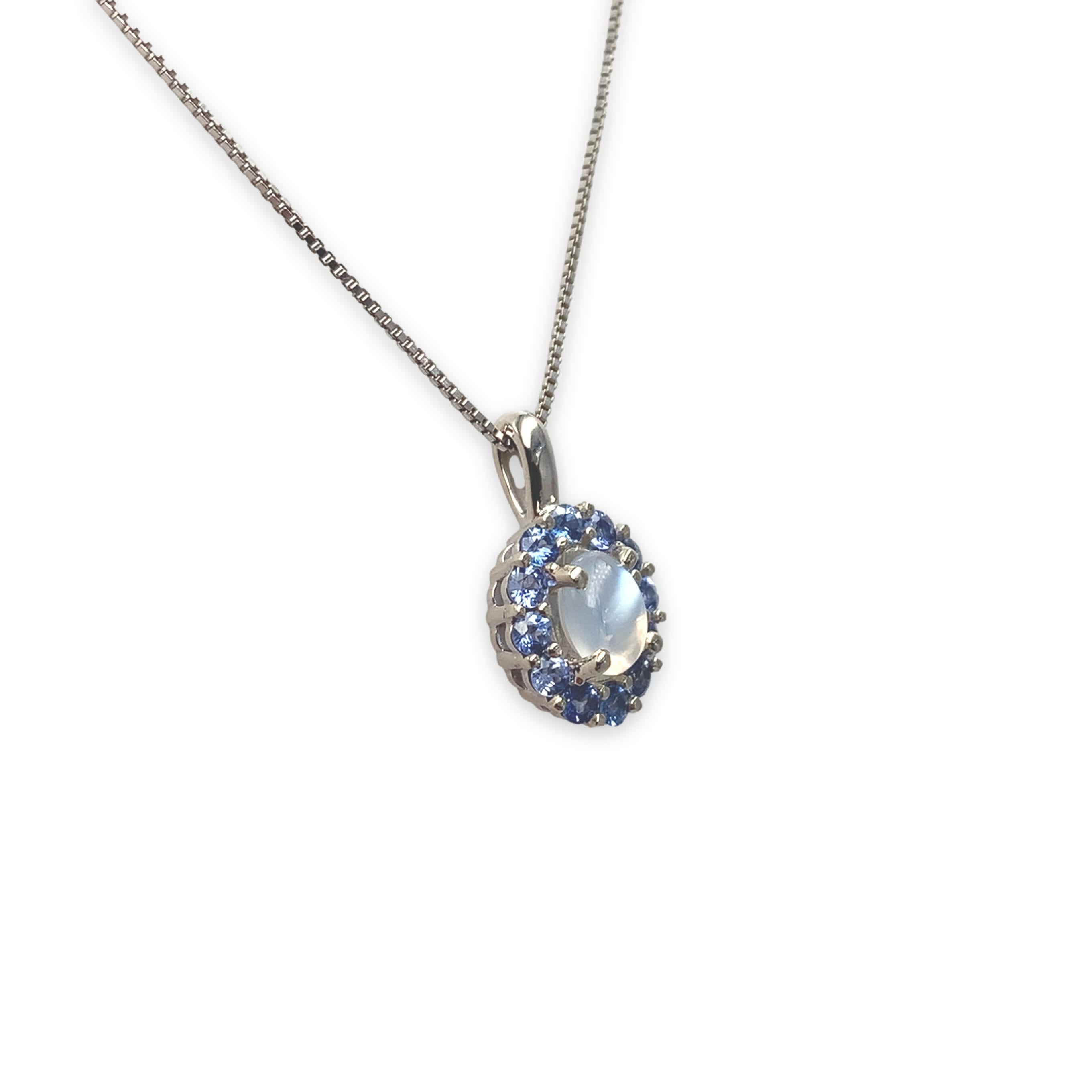 14K white gold moonstone and blue sapphire pendant. The genuine earth mined oval cabochon cut Ceylon moonstone is semi-transparent and has blue flash. It measures about 9mm x 7mm and weighs 1.25 carats. There are 12 natural earth mined lighter