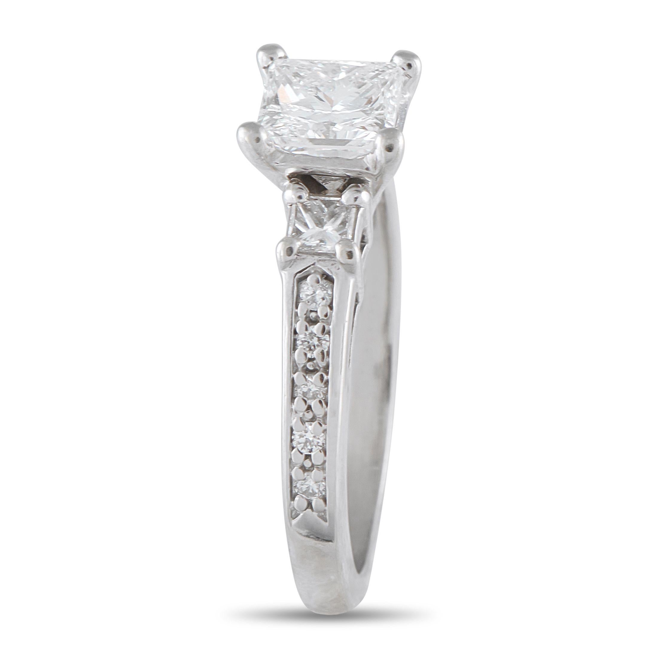 Este anillo de diamantes de oro blanco de 14 quilates aúna un diseño atemporal y un brillo resplandeciente. El anillo lleva una piedra central de diamante talla princesa de 1,03 ct de color G y claridad VS2. Flanqueado por dos diamantes más pequeños