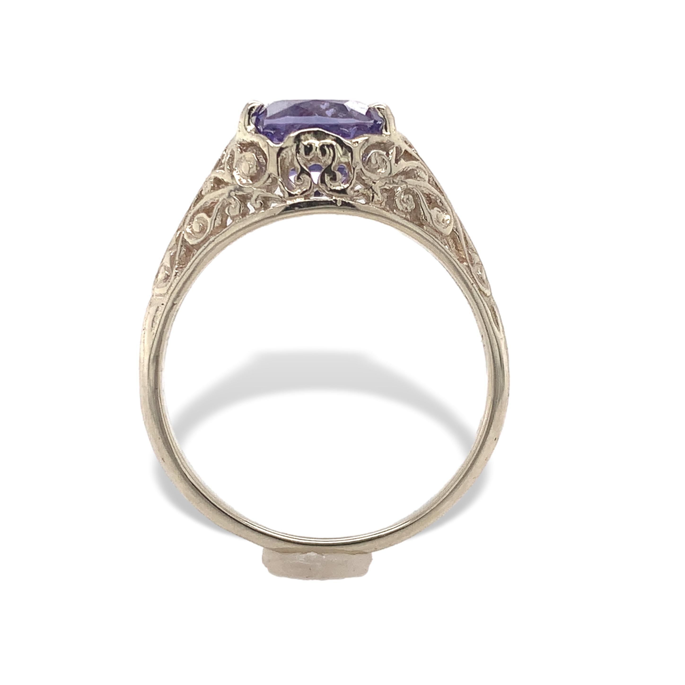 14K white gold purple sapphire filigree ring. The ring features a genuine earth mined oval cut purple sapphire. It measures 6.4mm x 5.3mm and weighs 1.43 carats. The sapphire has a CSL card stating natural unheated. The pierced filigree mounting