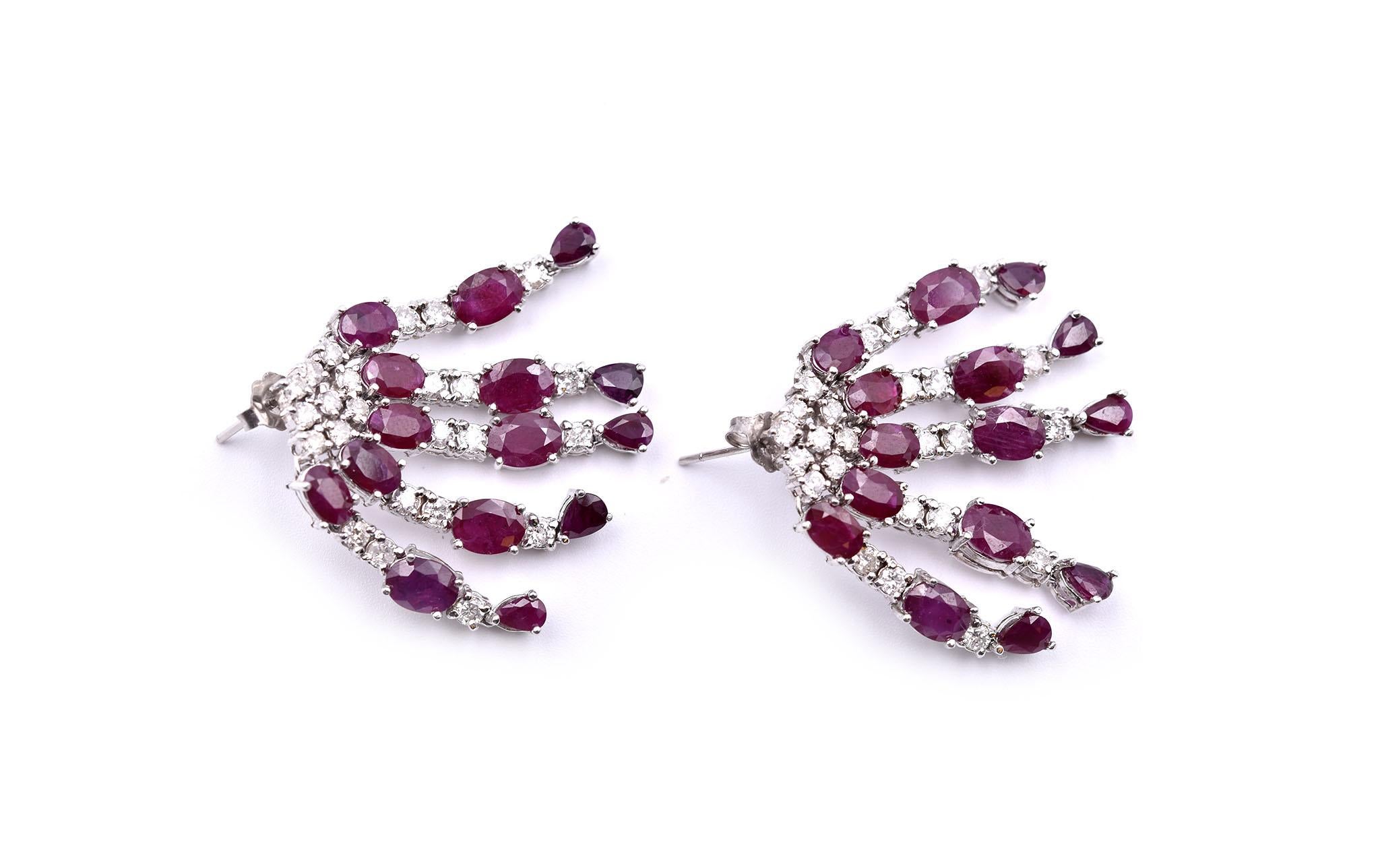 These earrings are crafted in 14k white gold. They feature five rows of diamonds and rubies hanging from a cluster of diamonds. There are 20 oval rubies and 10 pear rubies which have a total weight of 12.50cts, and 33 round diamonds which have a