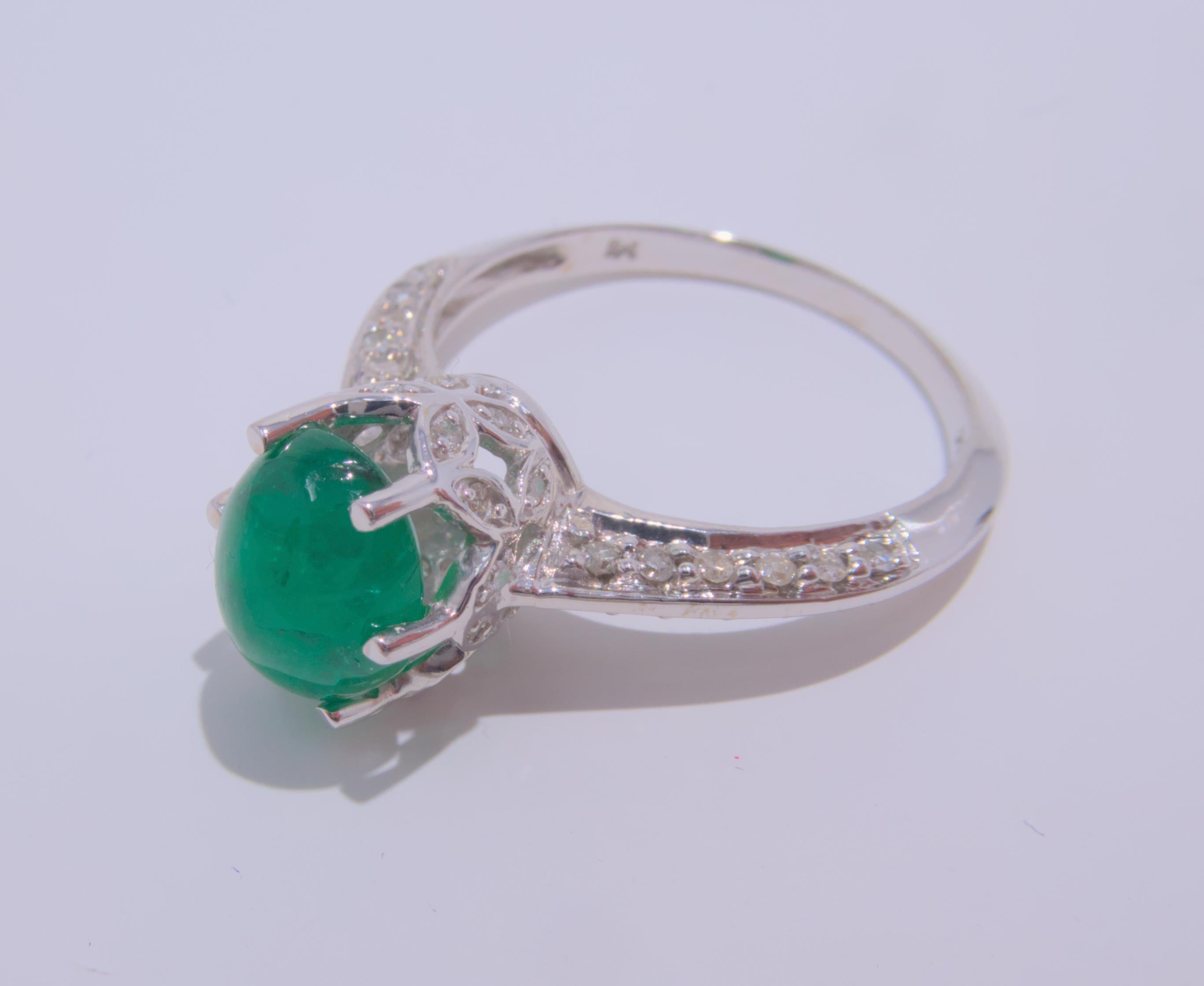 This stunning 14K white gold ring showcases a beautiful cabochon emerald at its center, surrounded by sparkling diamonds. The total estimated weight of the emerald is an impressive 1.90 carats, making it the perfect statement piece. The diamonds,