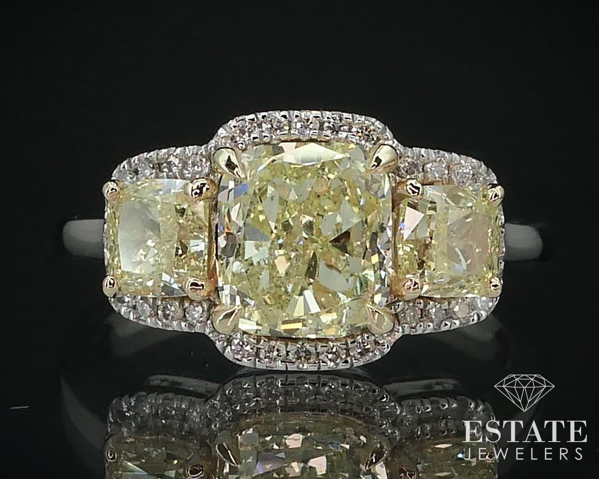 Beautiful three stone engagement ring with rare cushion cut fancy yellow colored main and side diamonds. Approximate 1.83ct on the main diamond with .60ctw with the two side accents. VS-I1 clarity to them. Small white diamonds act as a halo to the