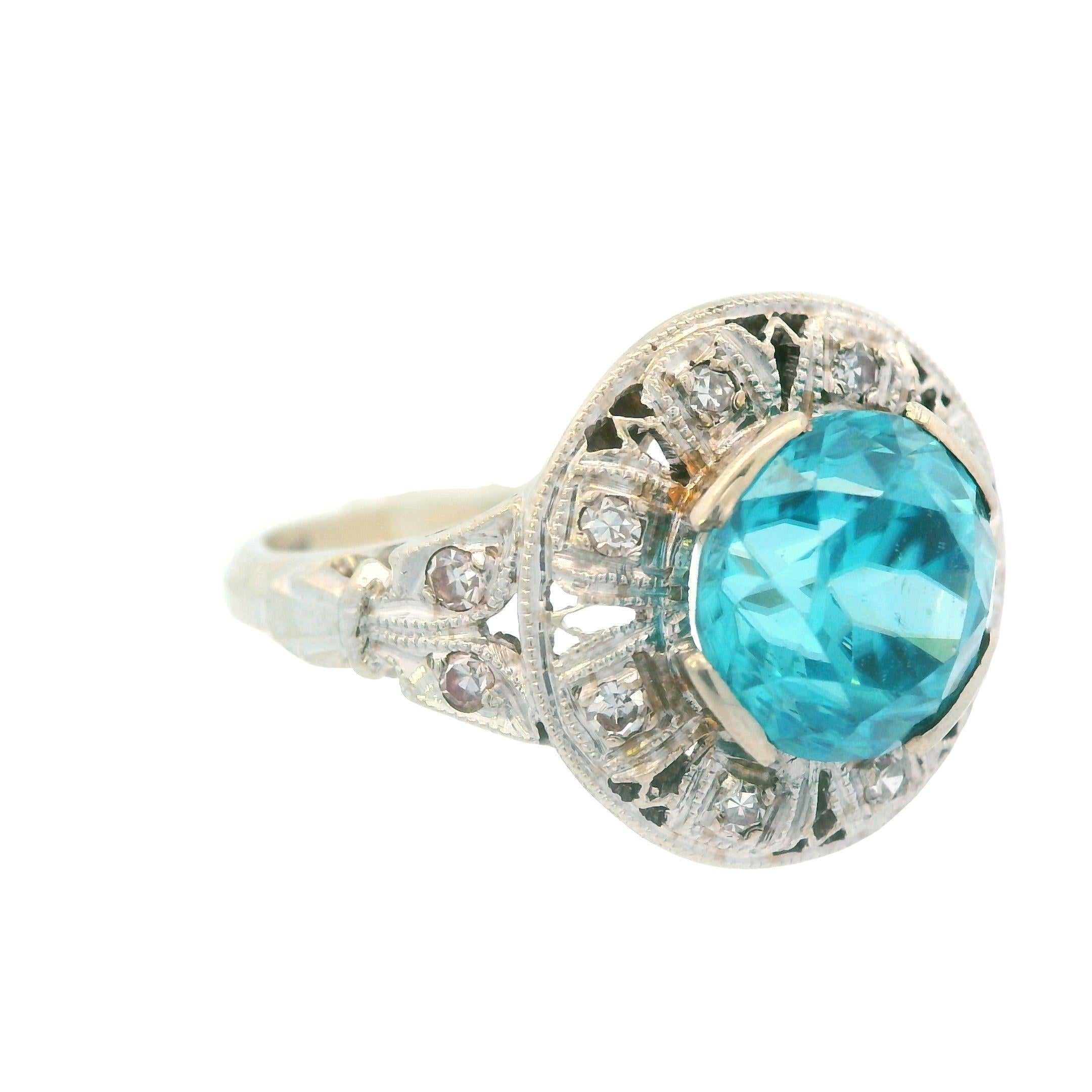 Cette séduisante bague Art déco en or blanc 14 carats est ornée d'un époustouflant zircon bleu de 3 carats entouré de diamants étincelants. Regarder le zircon de 3,00 carats de cette bague Art déco accrocheuse, c'est comme contempler un océan bleu