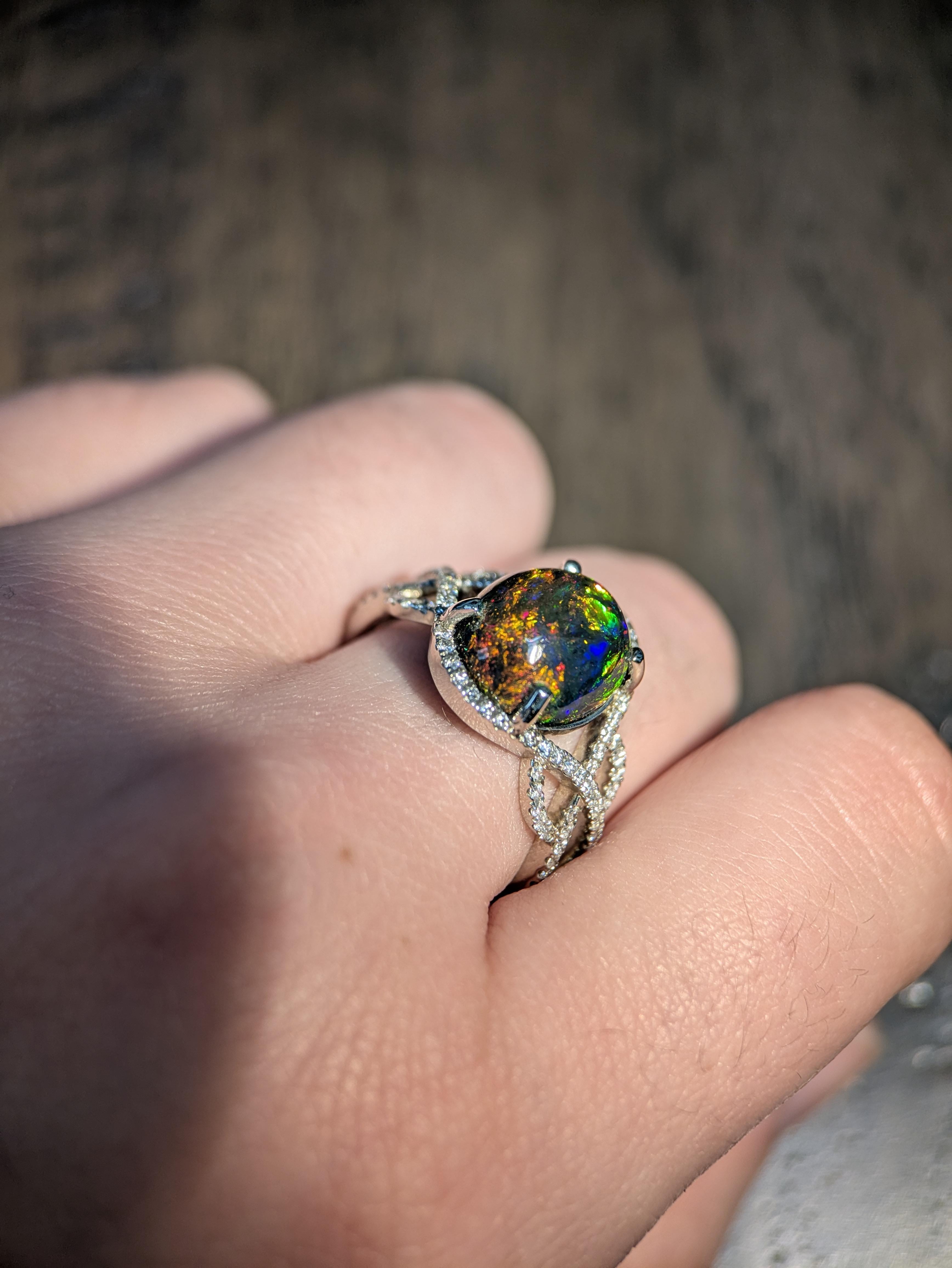 Elegante e accattivante, questo splendido anello ha come pietra centrale un opale nero ovale da 3,35ct (12x10mm) che mostra vividi giochi di colore. Incastonata in oro 14k (4g), l'opale è circondata da 86 diamanti scintillanti per un totale di