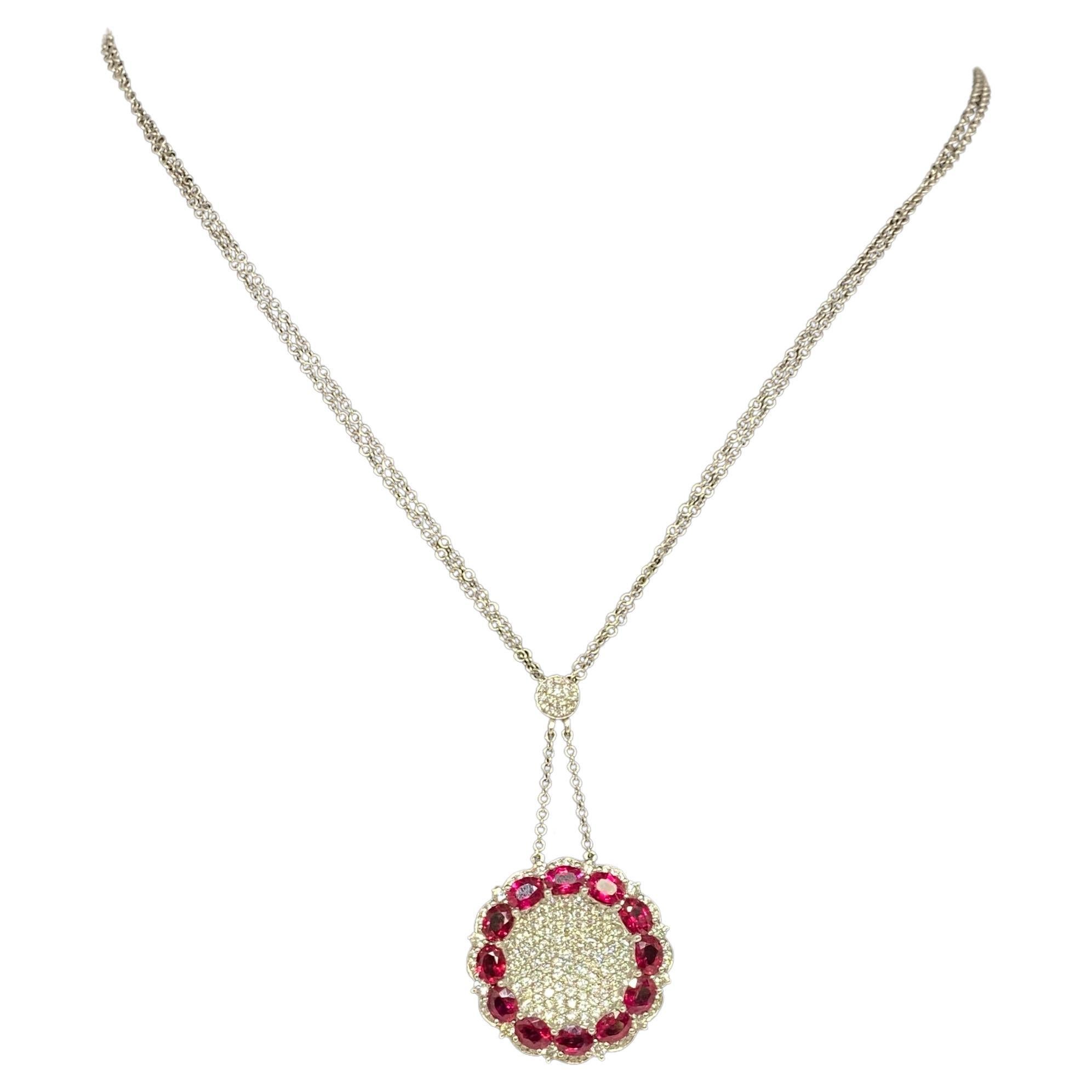 This 14k white gold necklace features a beautiful and striking round concave disc encrusted with sparkling natural round brilliant cut diamonds and a contrasting halo of larger oval vivid natural red rubies suspended from a small diamond cluster. 