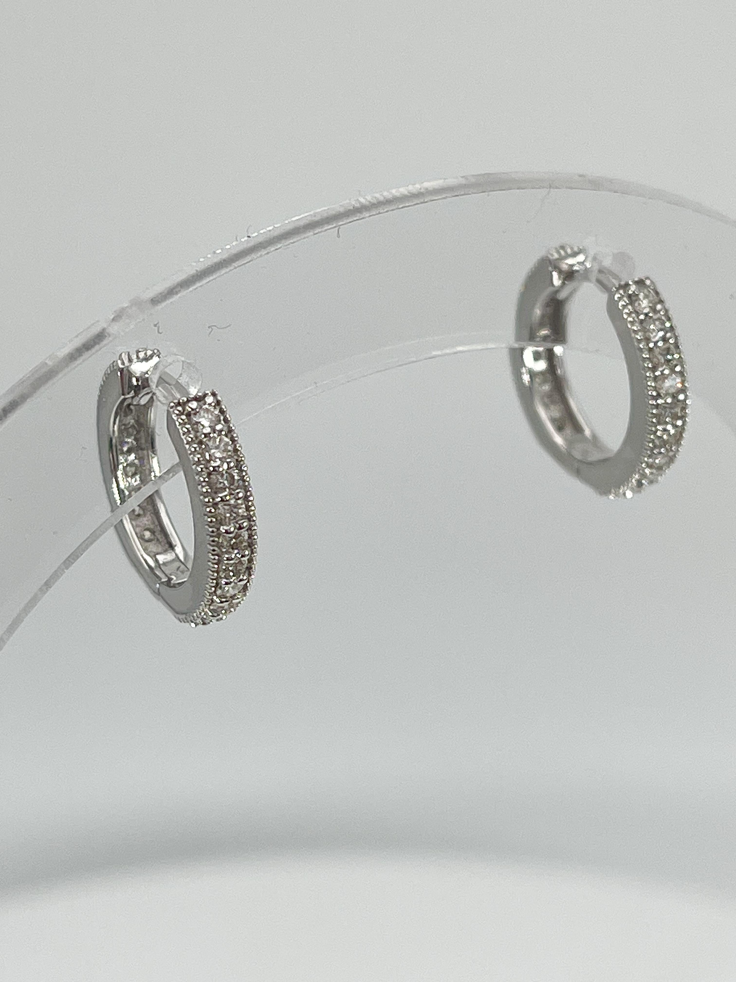 14k white gold .60 CTW diamond huggie hoop earrings. These earrings have diamonds on front and back side, all the stones are round, they measure to be 14mm x 2.7mm, and they have a total weight of 2.3 grams.