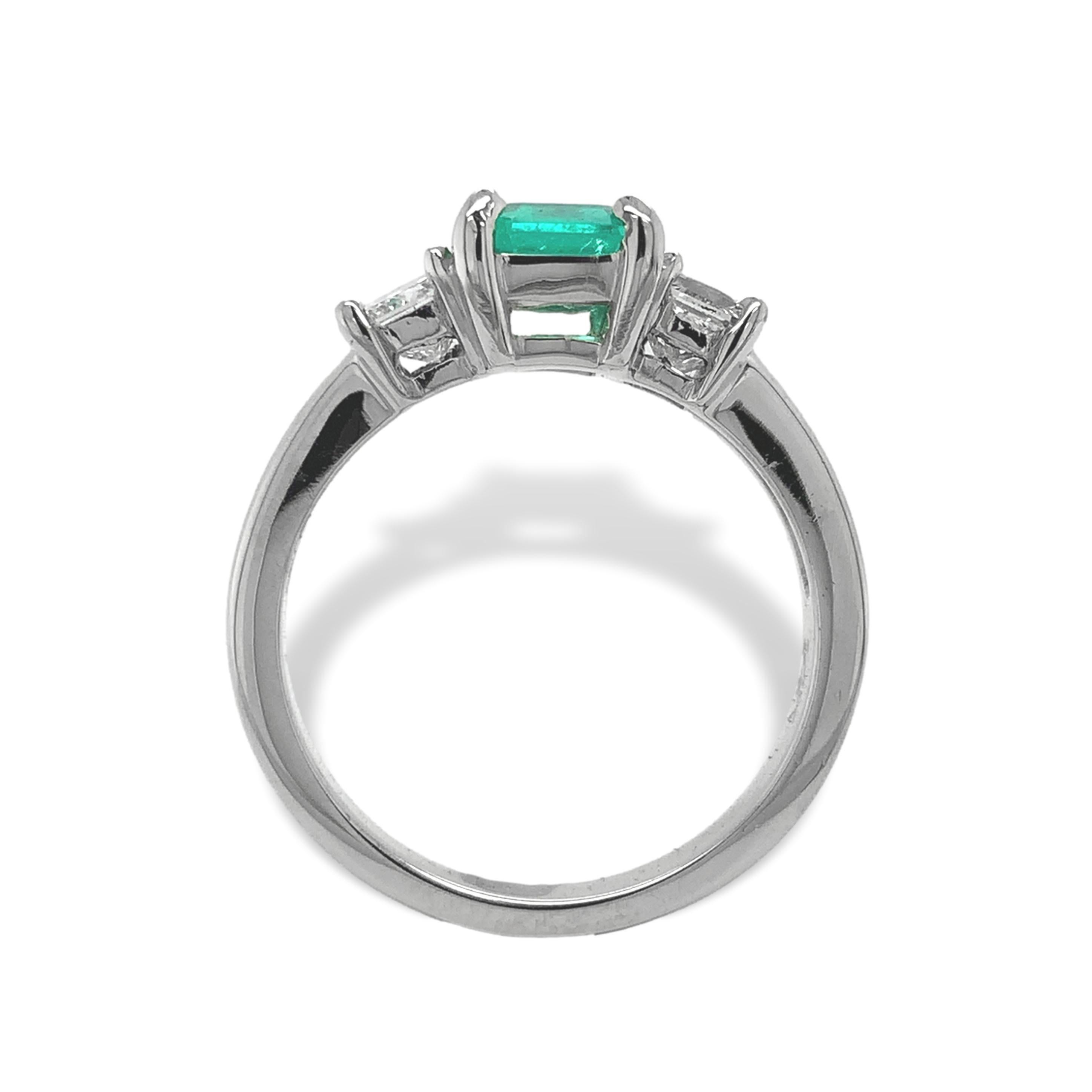 14K white gold ring featuring an emerald cut Colombian emerald weighing .90cts. The genuine earth mined emerald has light bright grass green color and measures 6.9mm x 6mm. There are 2 square brilliant cut diamonds weighing about .65cts total. The
