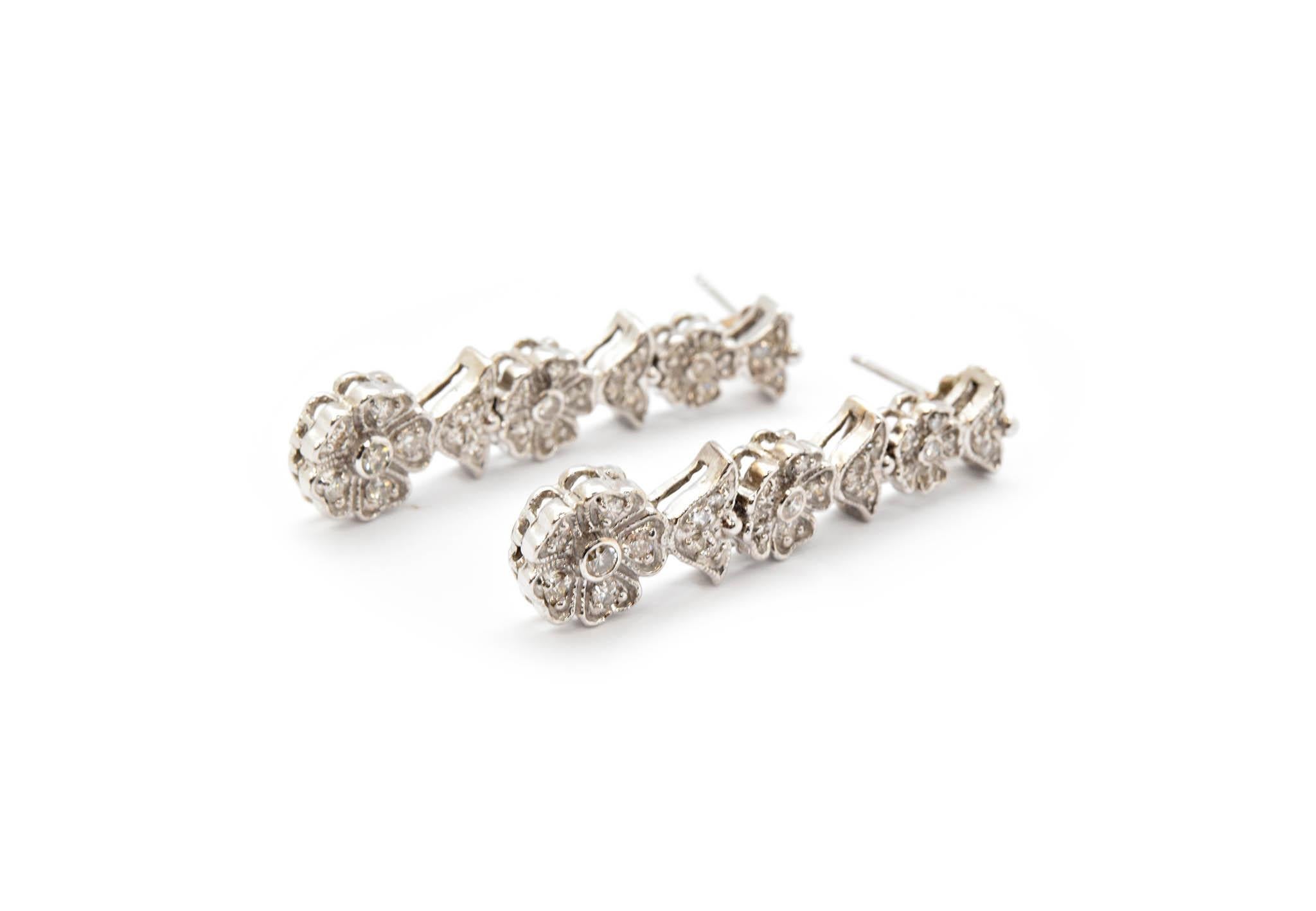 This pair of earrings is made in 14k white gold. It features a flower motif with each part of the flower set with round diamonds. The diamonds have a total weight of 1.28 carats, and the stones are graded G-H in color and SI in clarity. The earrings