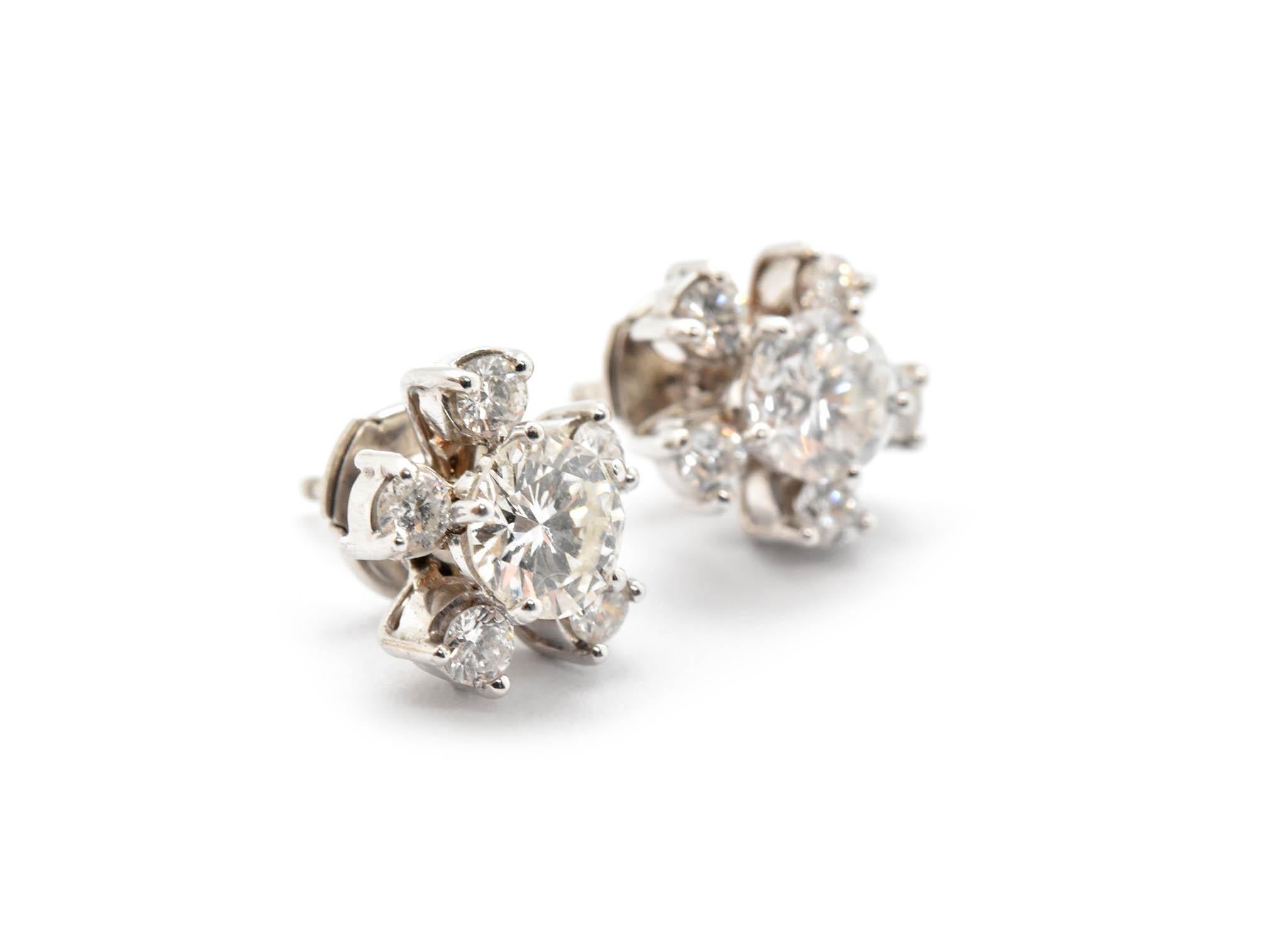 These stud earrings are made in 14k white gold. They feature two round, brilliant cut diamond center stones that have a total weight of 1.08ct. One diamond is graded J in color and SI1 in clarity. The other diamond is graded I in color and SI2 in