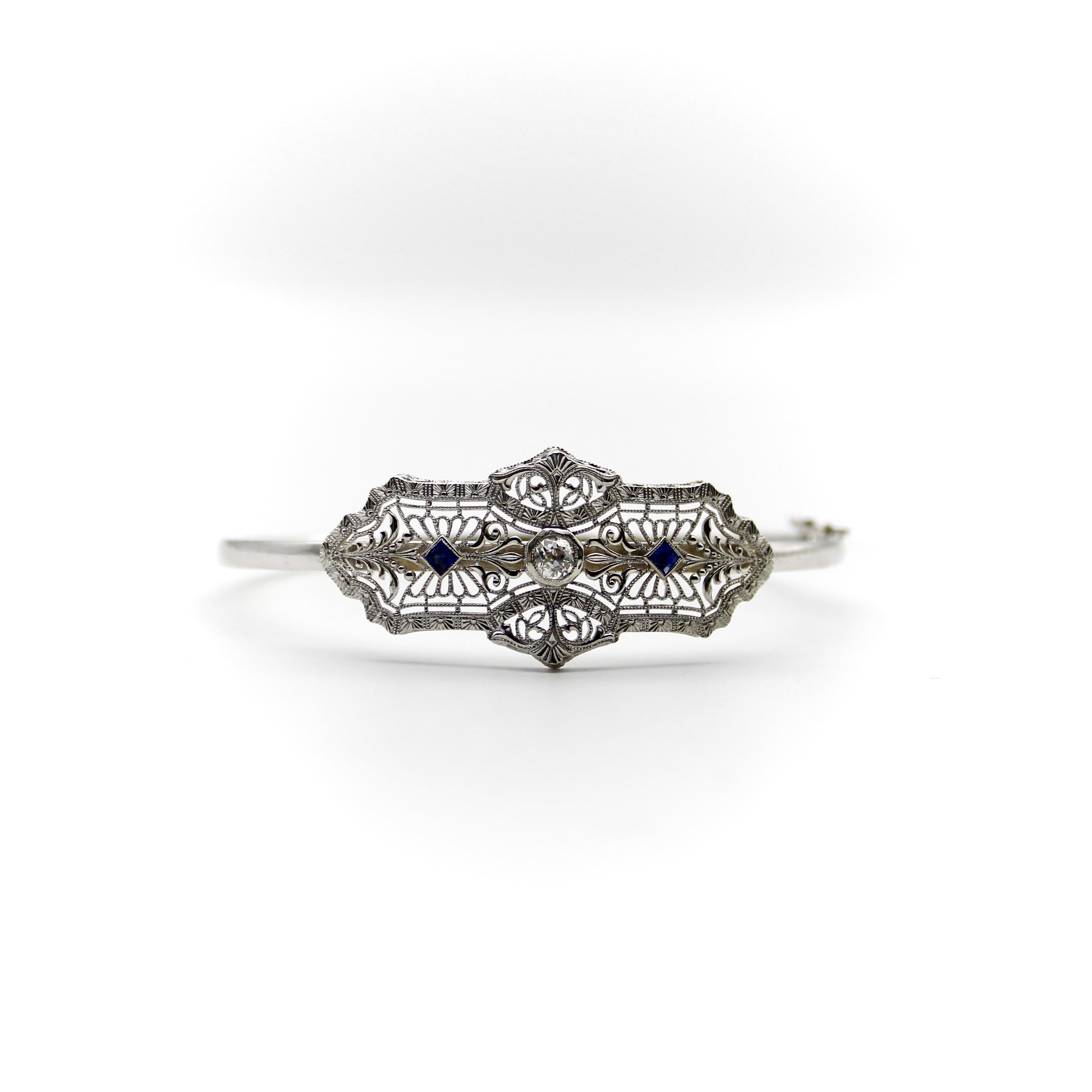 14K White Gold Art Deco Diamond & Sapphire Bracelet
 
A delicate Art Deco bracelet made of 14k white gold with a European cut diamond center and two French cut sapphires on the side. The centerpiece has a symmetrical design, filled with delicate