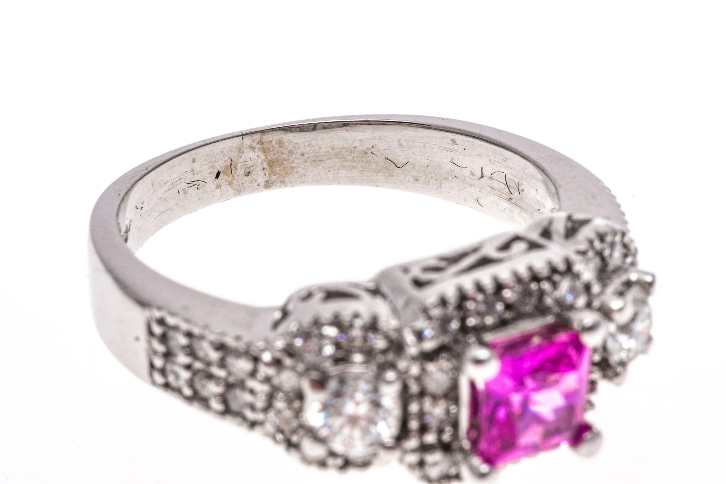 14k white gold ring. This beautiful ring features a center square faceted, medium pink color pink sapphire, approximately 0.47 CTS, decorated with a round faceted diamond halo. The pinks sapphire is flanked by round brilliant cut diamonds, also