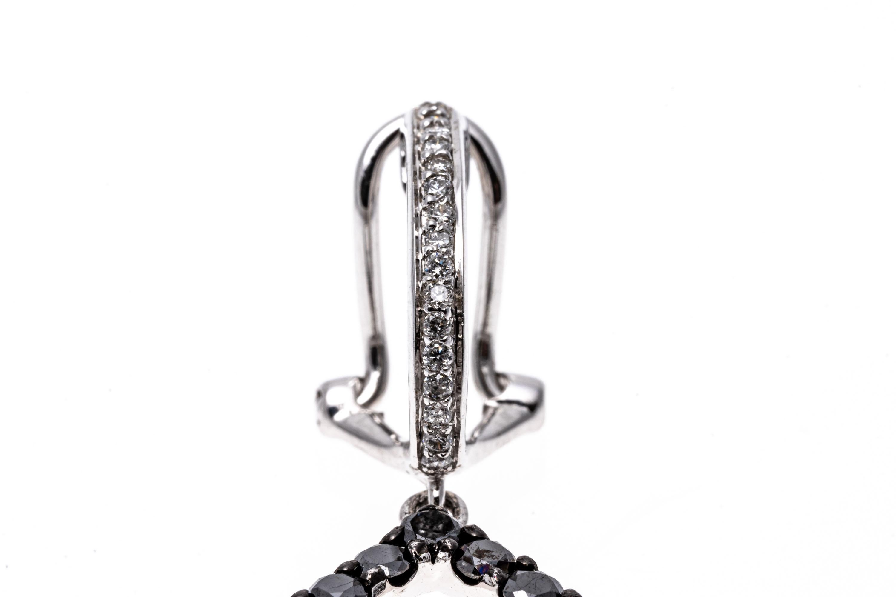 14k white gold earrings. These beautiful earrings contain a small hoop top, set with a row of round faceted, white diamonds. Suspended from the hoop is a pear shaped open drop style pendant trimmed with round faceted, black diamonds, prong set. The