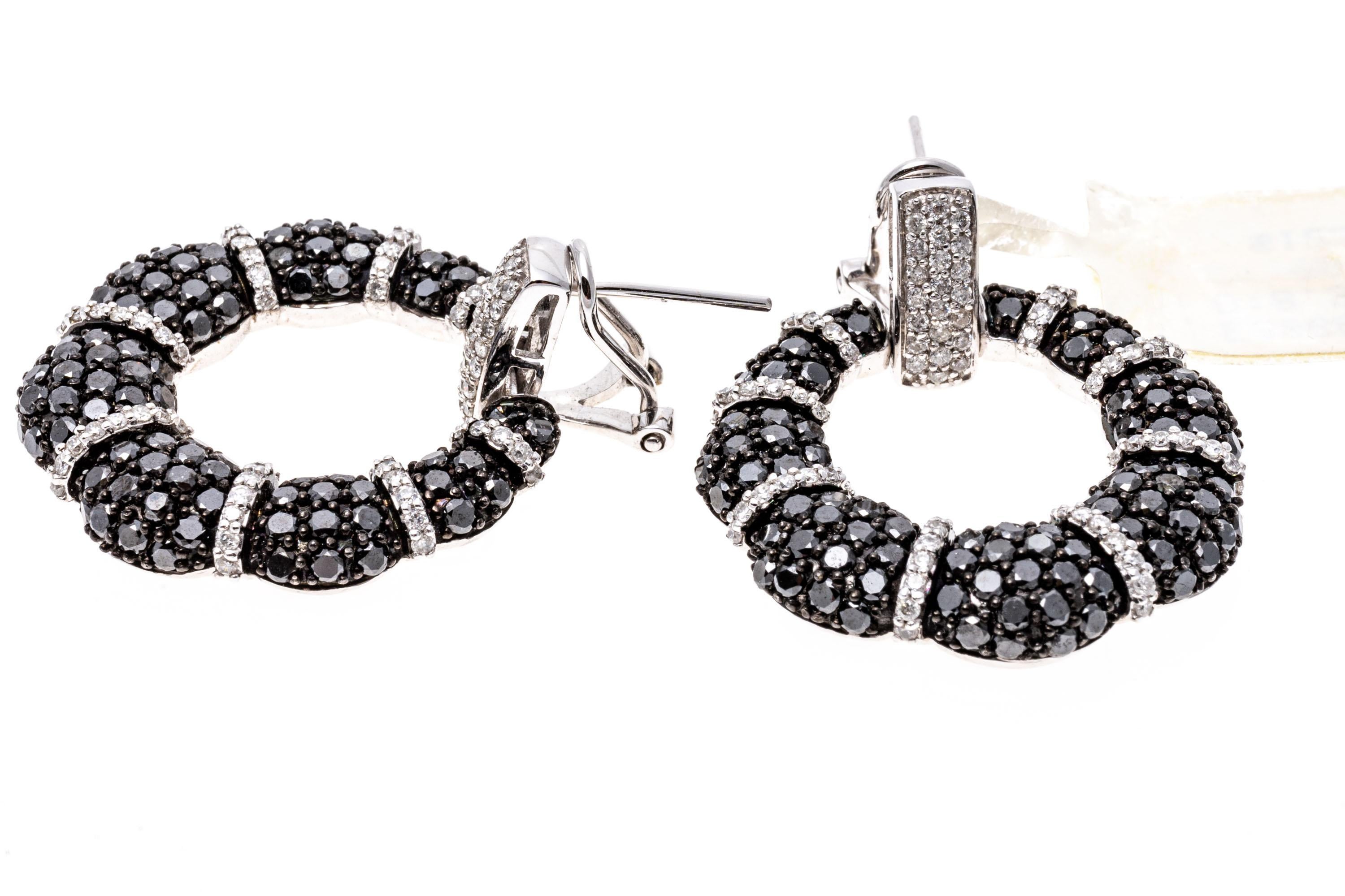 14k white gold black and white diamond earrings. These striking earrings are a doorknocker style, with a wreath-like bottom, and are pave set with round black diamonds alternating with a white round diamond trim, 8.35 TCW. The earring have posts
